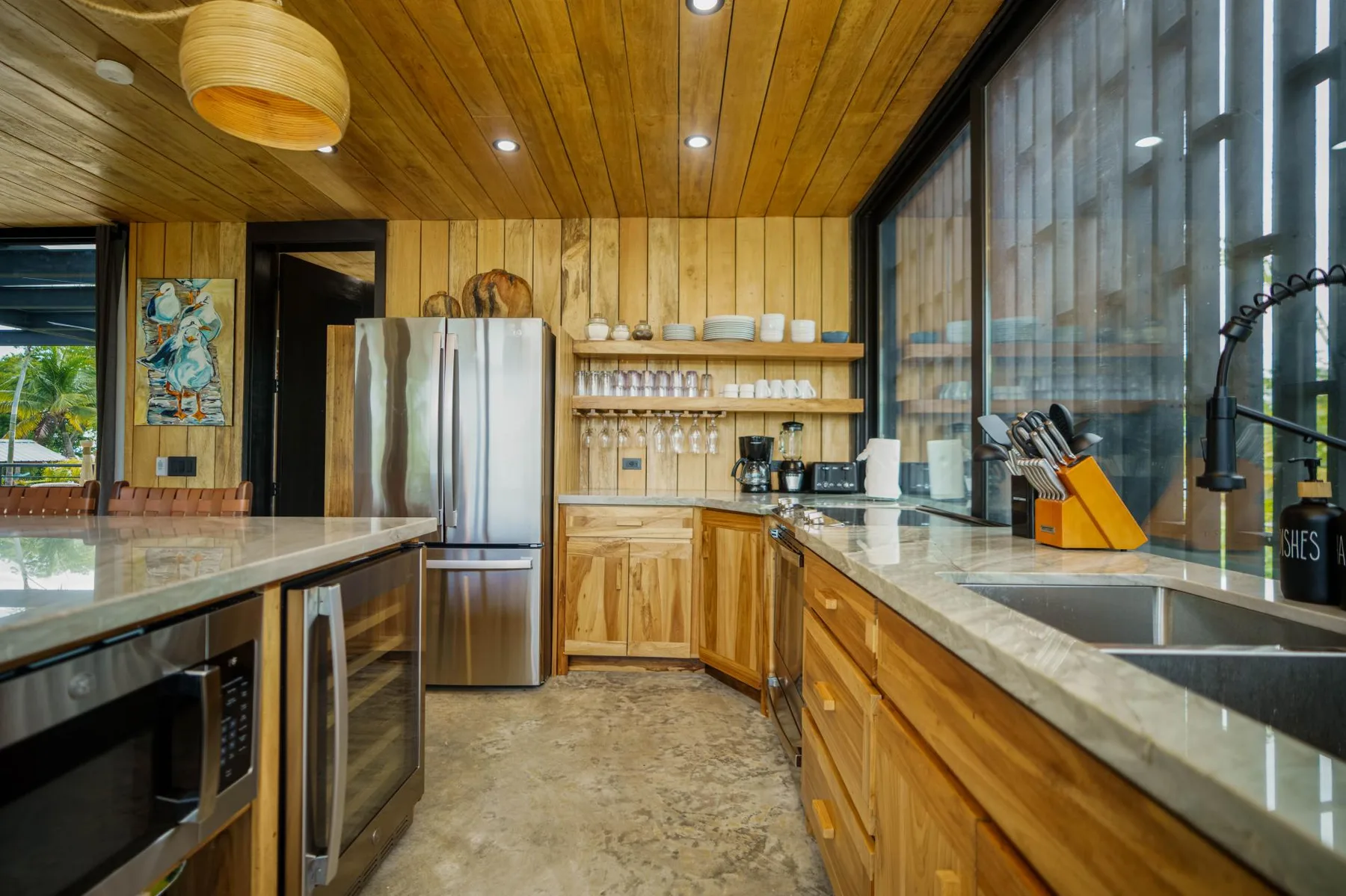 A spacious kitchen with wooden cabinets, stone counters, and large windows.