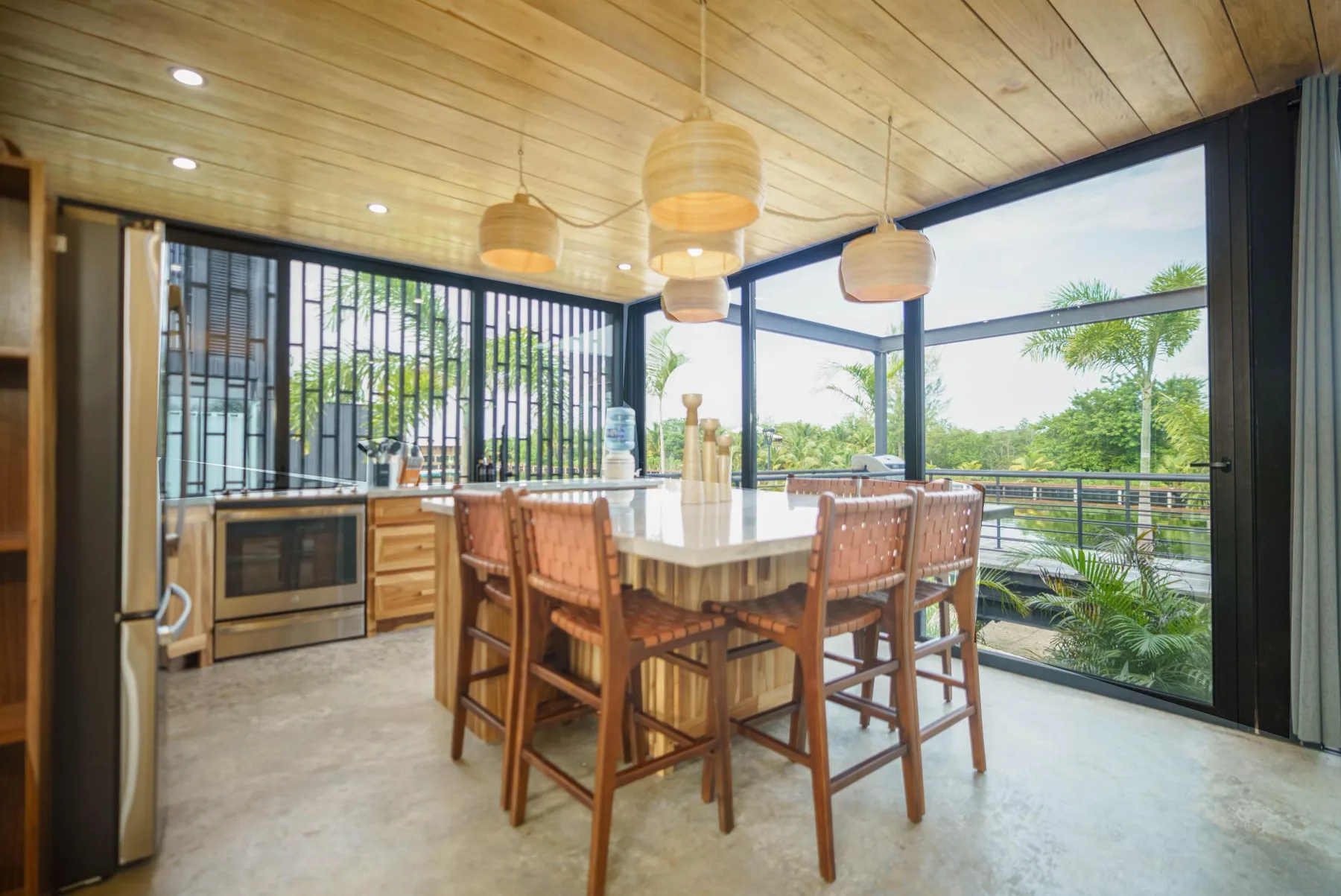 A dining area with a long table and large windows overlooking greenery.