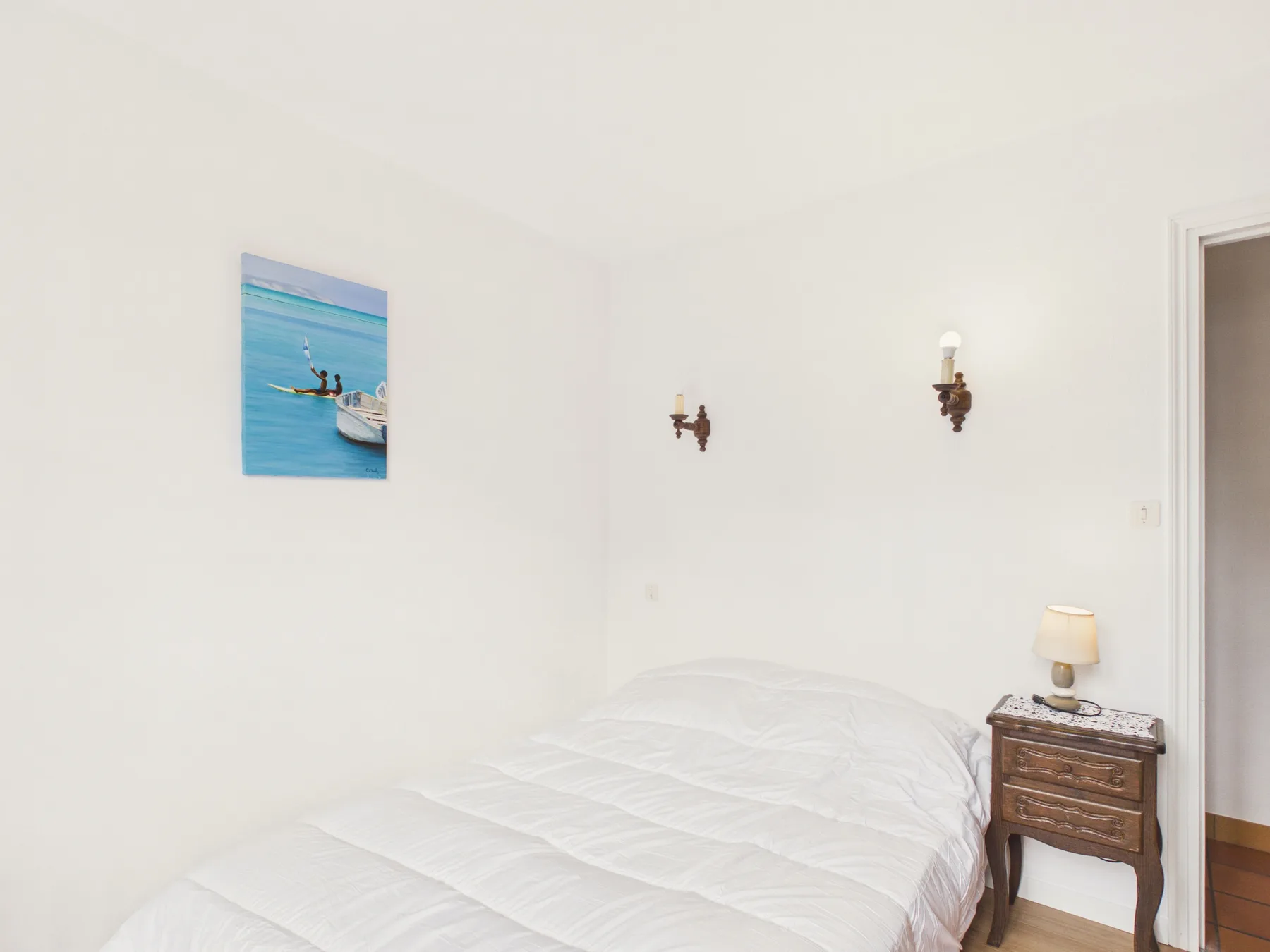A bright bedroom with a neatly made bed and a small bedside table.