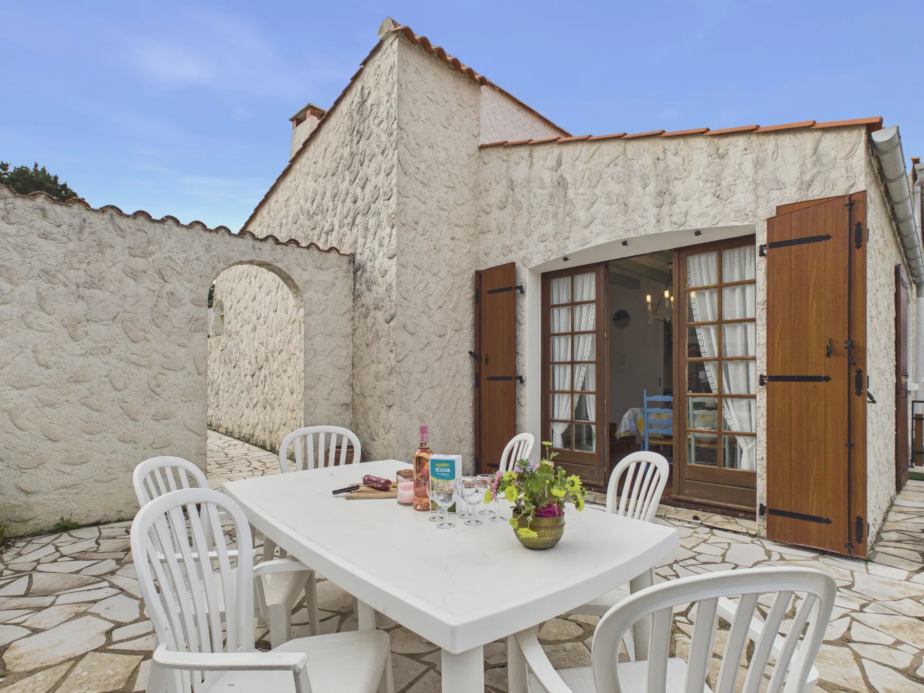 An outdoor dining area with a white table and seating beside an open doorway.