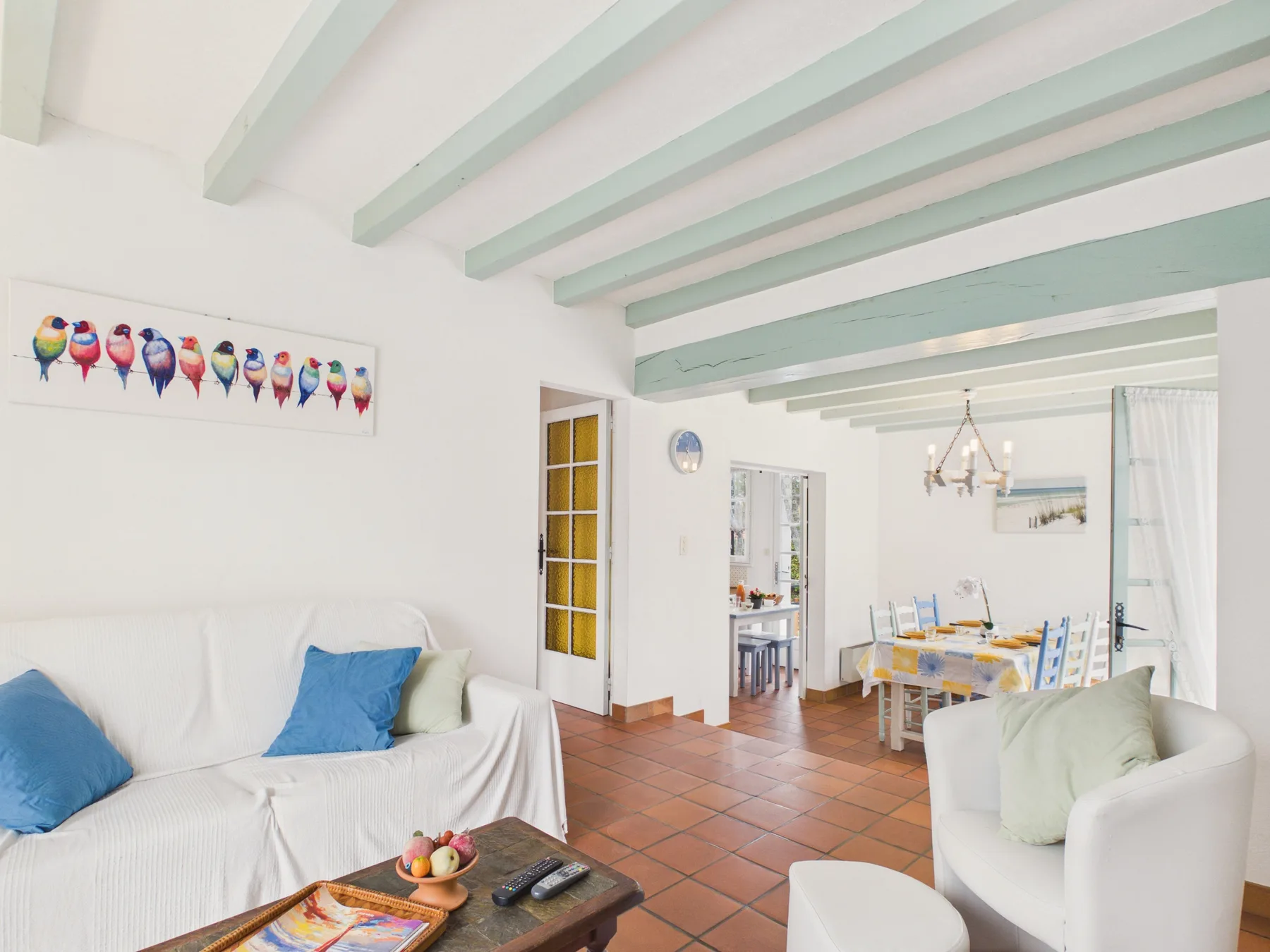A bright living and dining area with white seating and mint-colored ceiling beams.