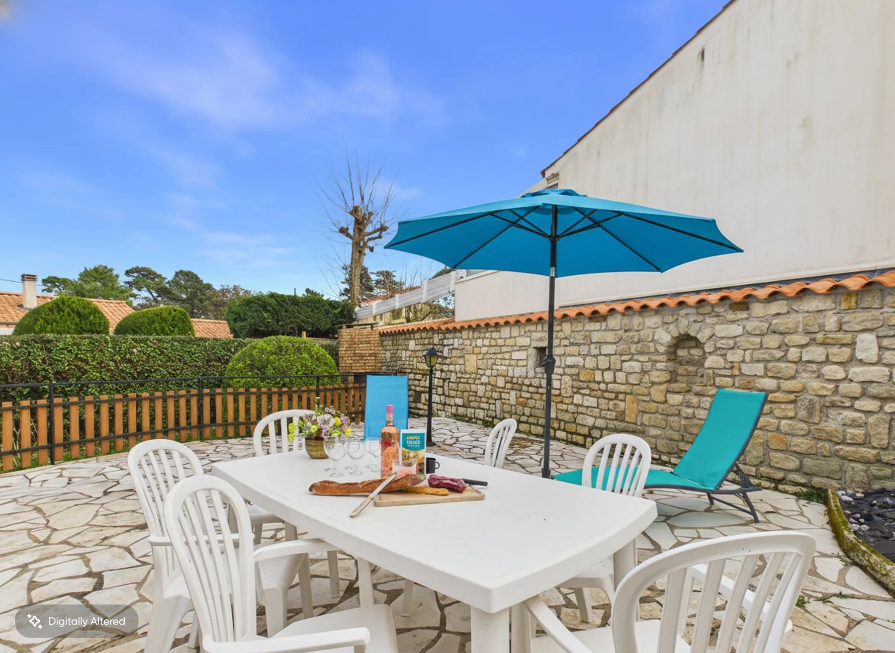 A stone-paved outdoor dining area with a table, chairs, and a blue umbrella.