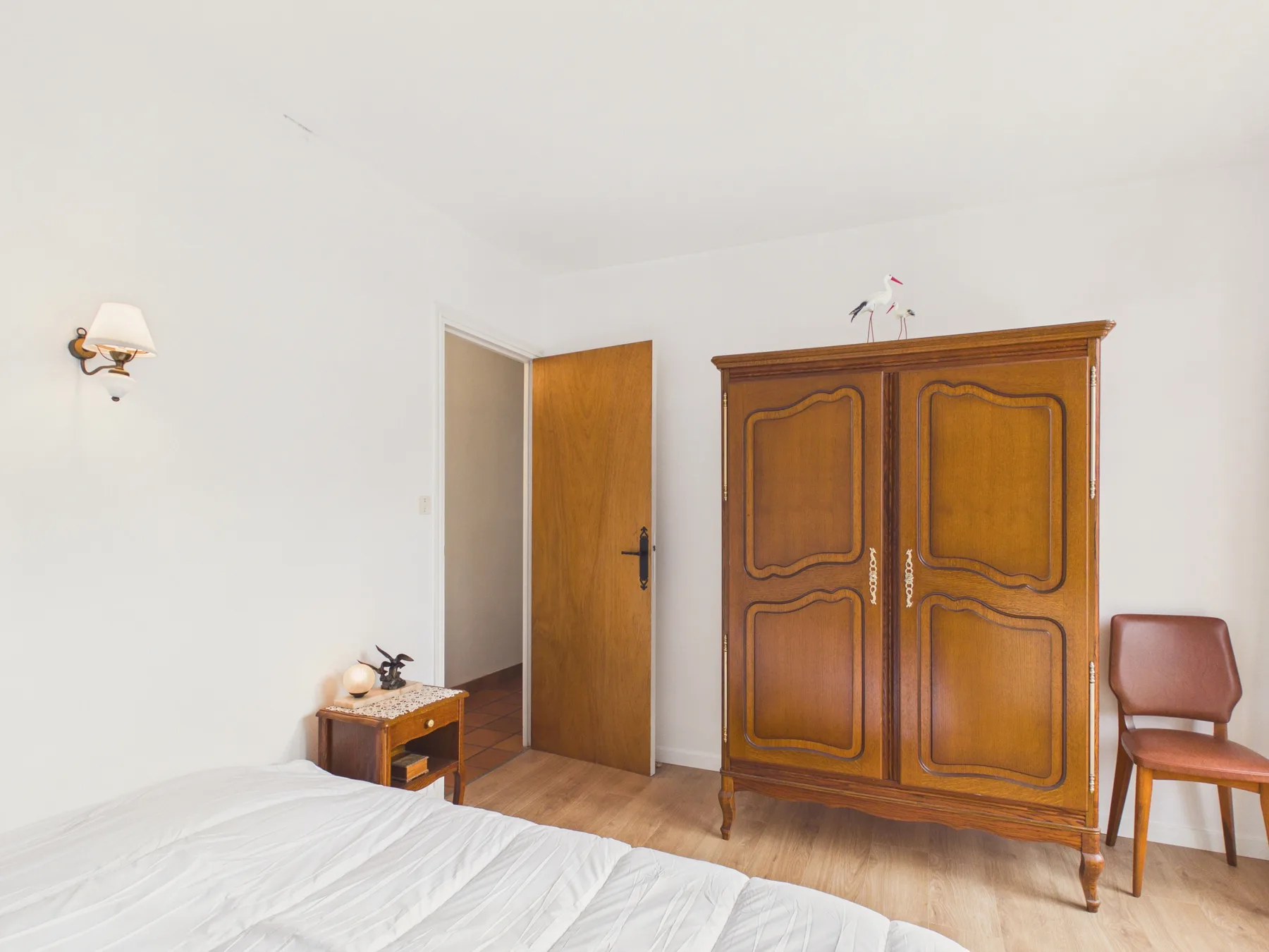 A bright bedroom with a wooden wardrobe and an open door.