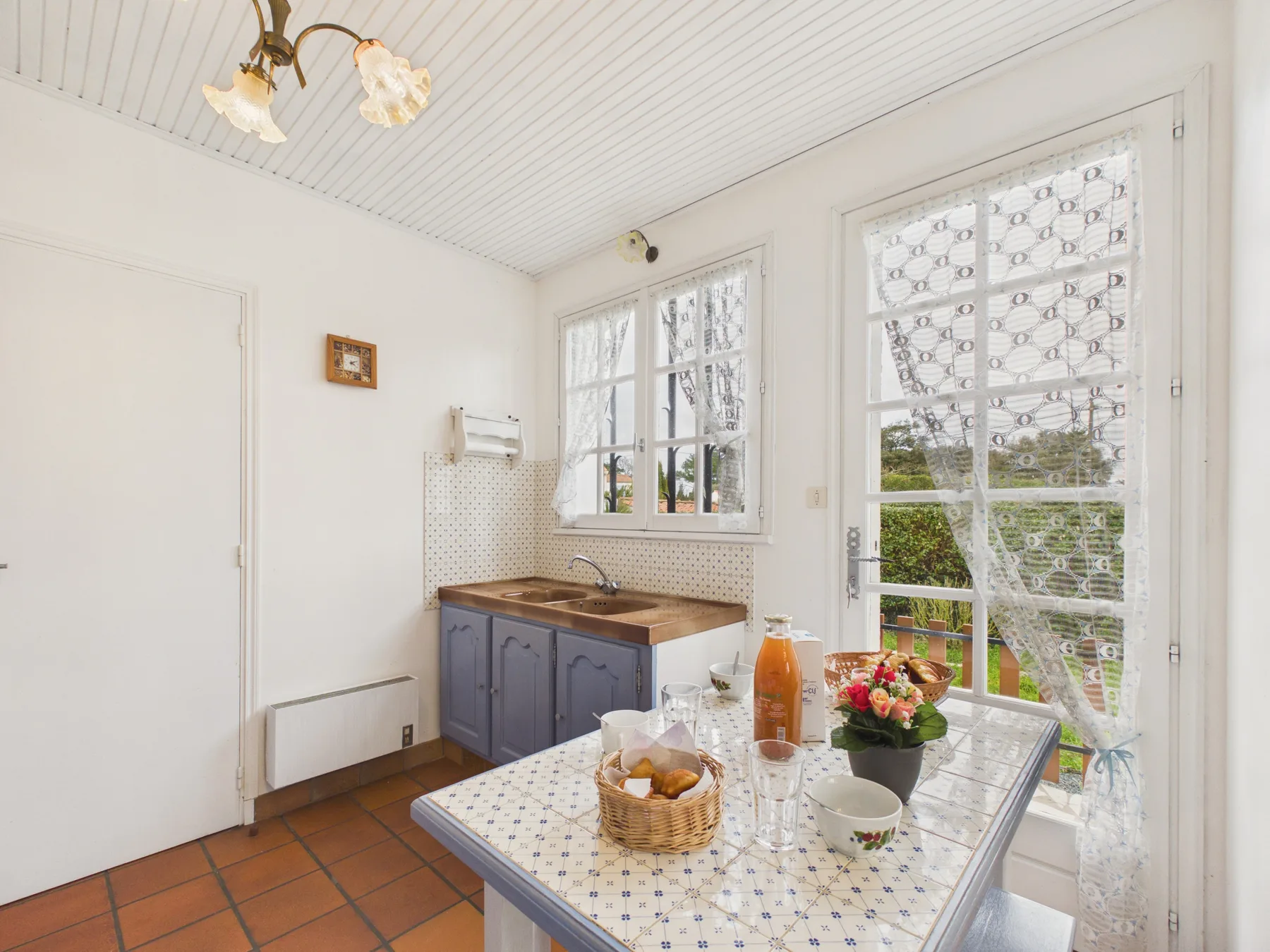 A bright kitchen with a tiled table and windows overlooking greenery.