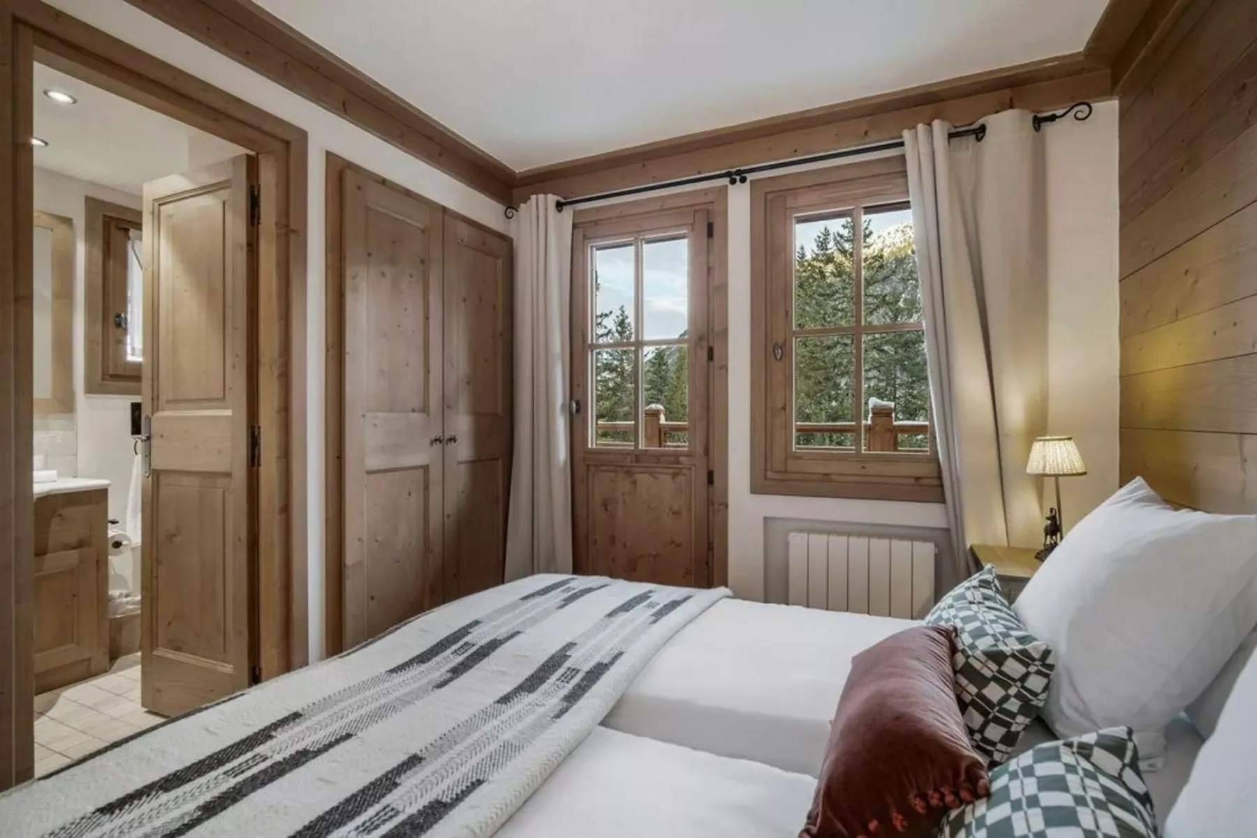 A bedroom with a bed, wooden wardrobes, and windows overlooking greenery.