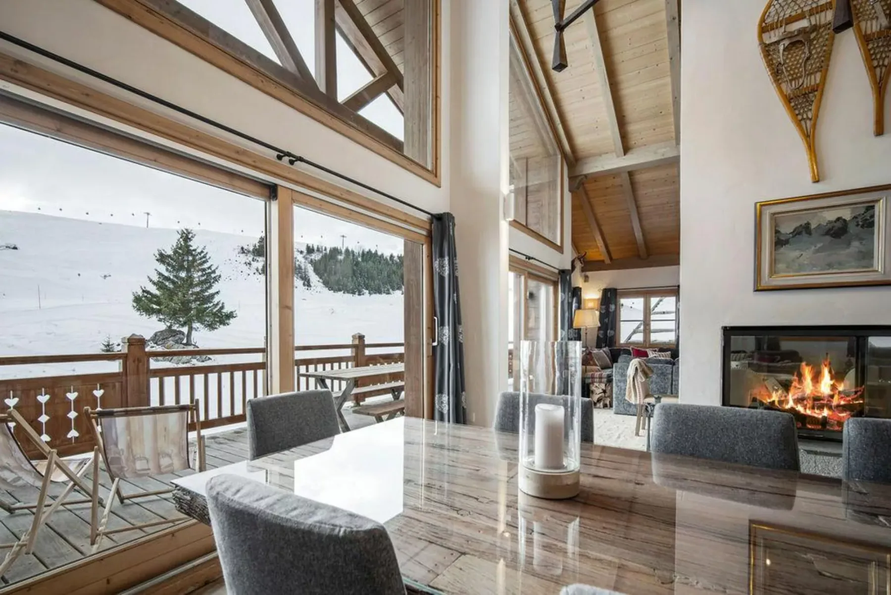 A dining area with large windows overlooking a snowy landscape and a fireplace nearby.