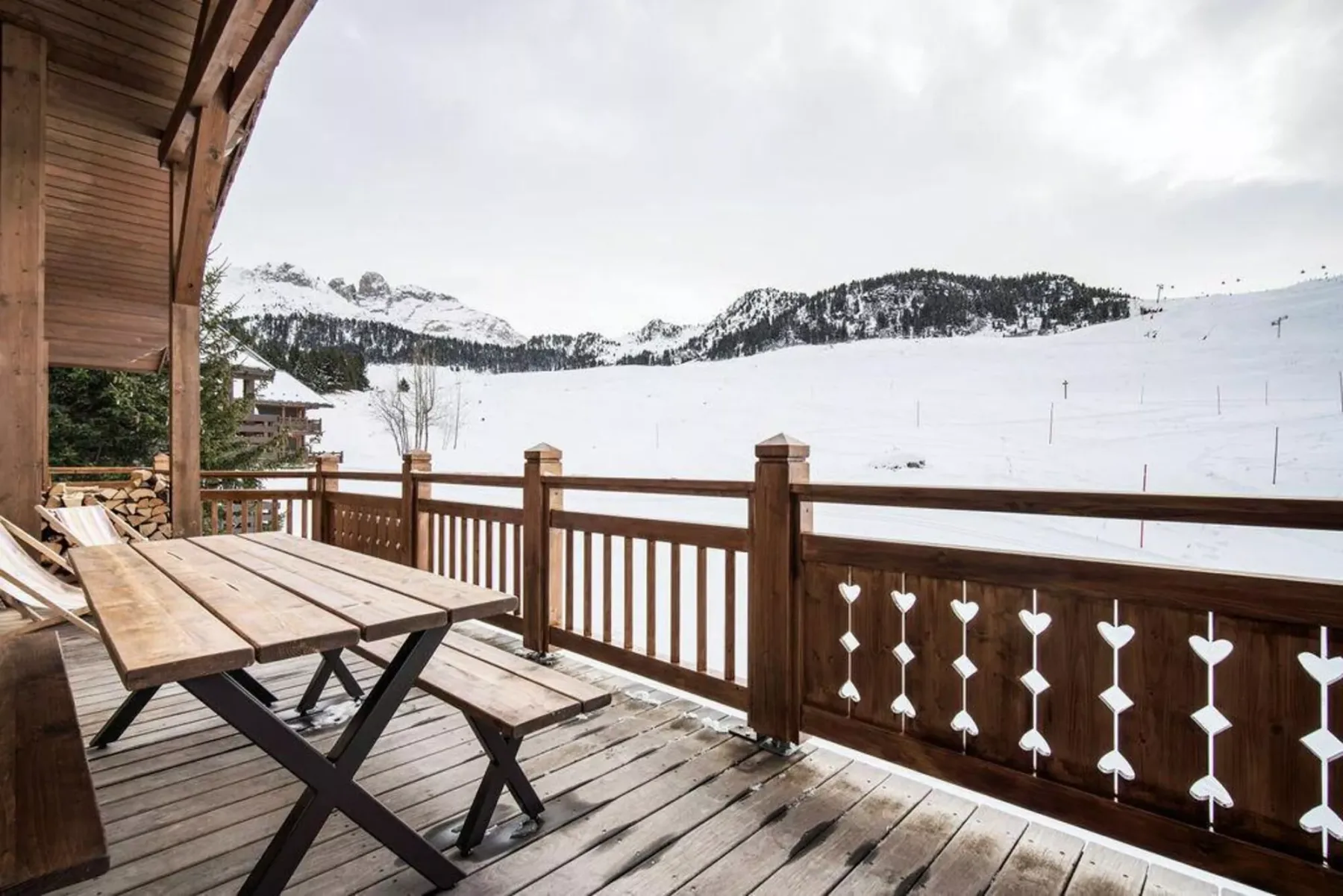 A wooden deck with outdoor seating overlooks a snowy mountain slope.