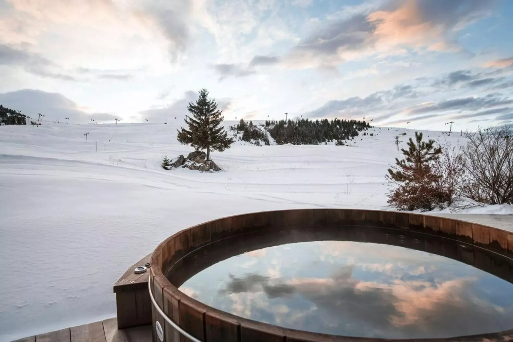 Una bañera redonda al aire libre da a un paisaje nevado bajo un cielo colorido.