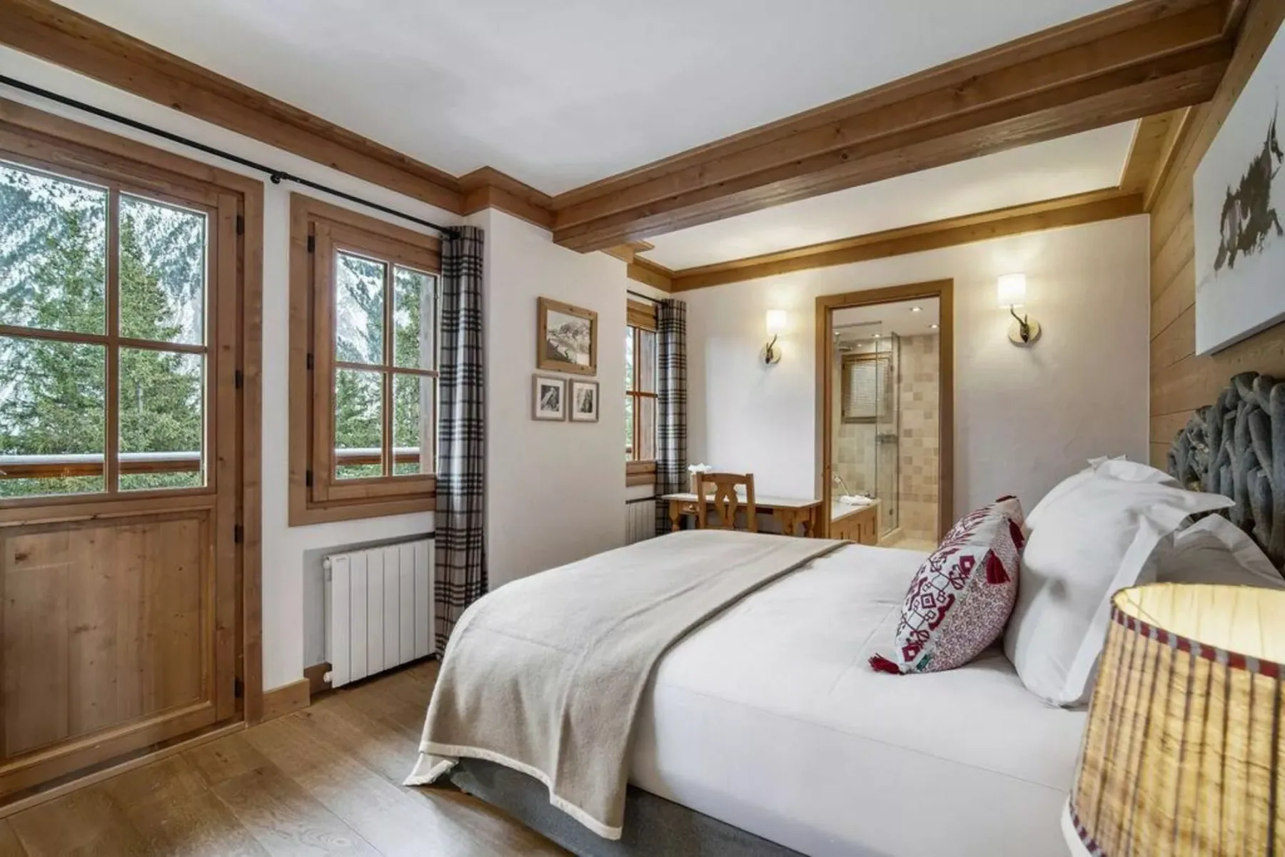 A bedroom with a large bed, wood-trimmed windows, and a small table.