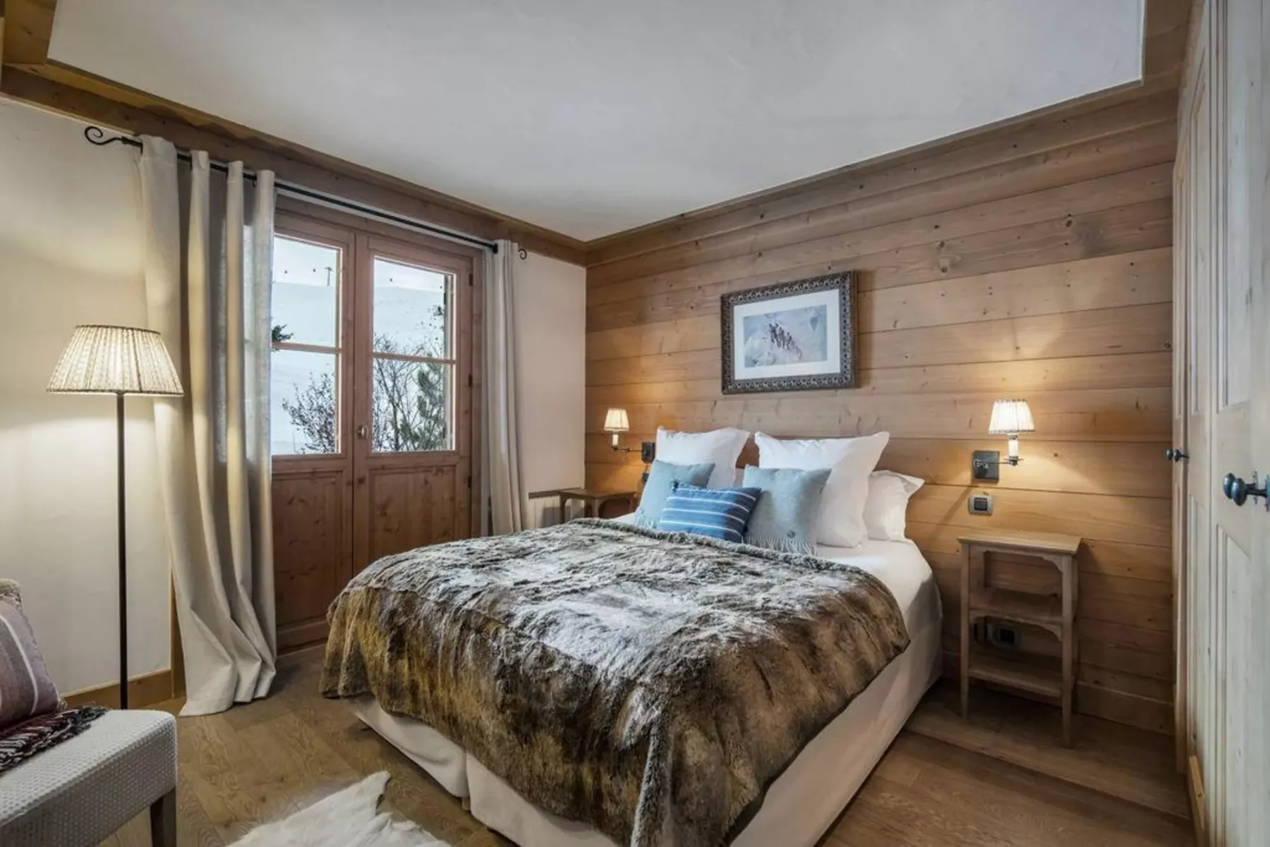 A bedroom with a bed, wood-paneled walls, and glass doors beside the bed.