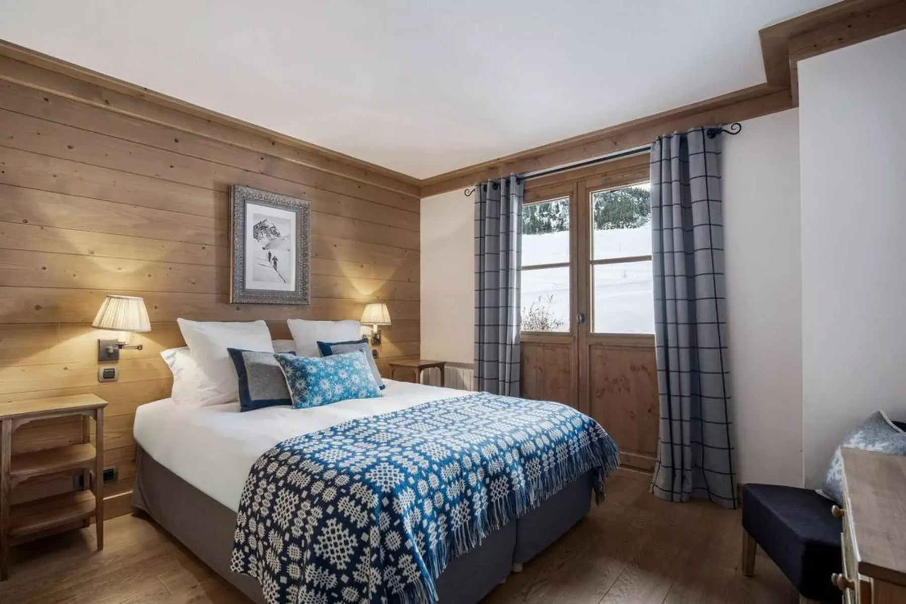 A bedroom with a bed covered in a blue patterned blanket beside wood-paneled walls.