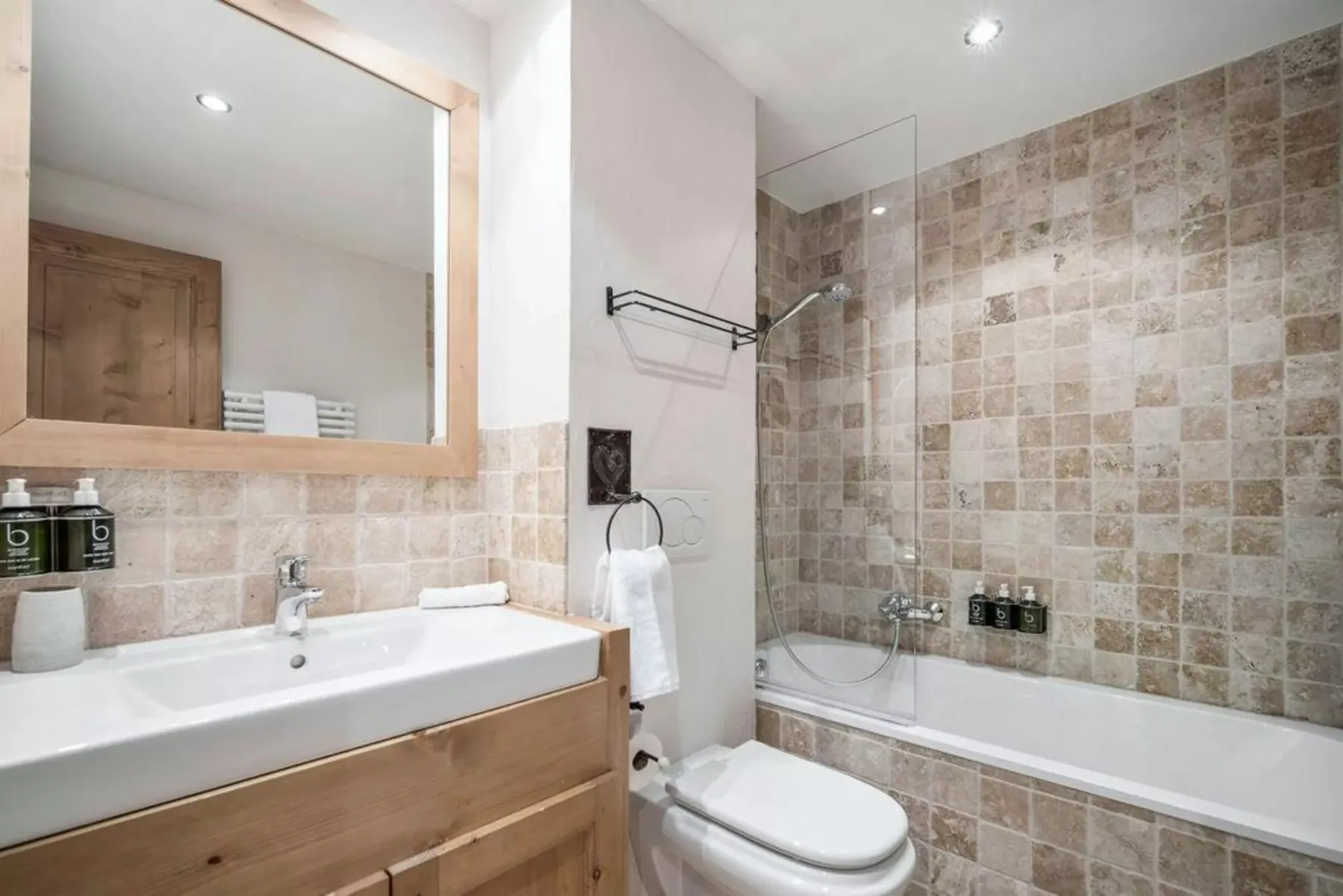 A bathroom with a sink, toilet, and bathtub with a glass shower screen.