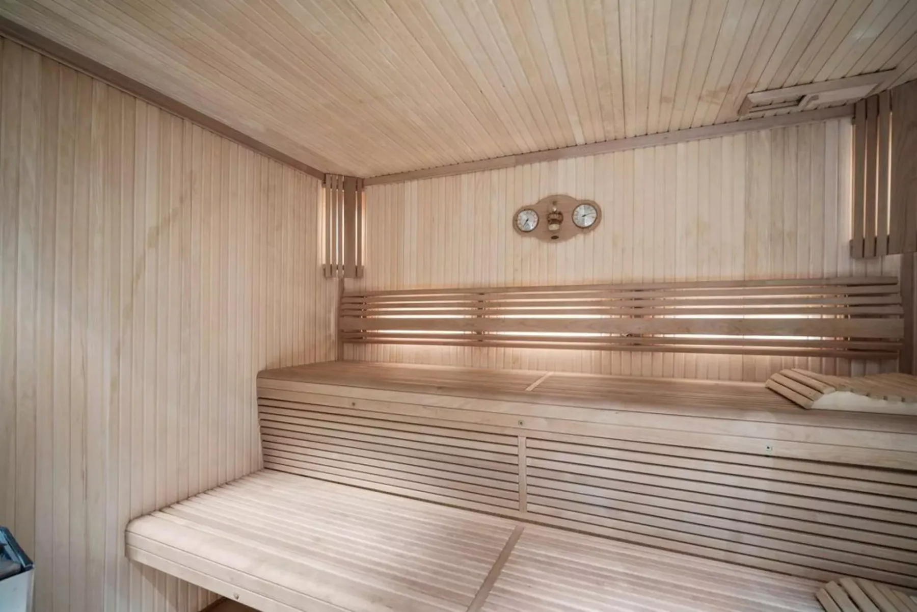 A wood-paneled sauna with tiered benches and a wall-mounted gauge.