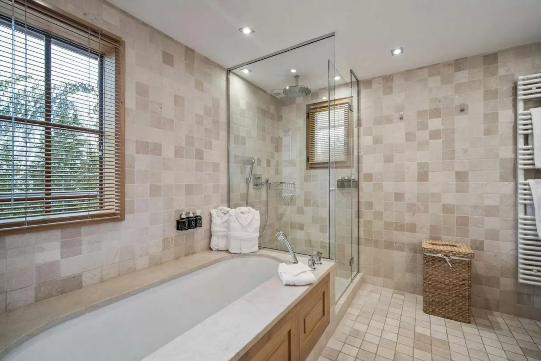 A tiled bathroom with a bathtub, glass shower enclosure, and window.