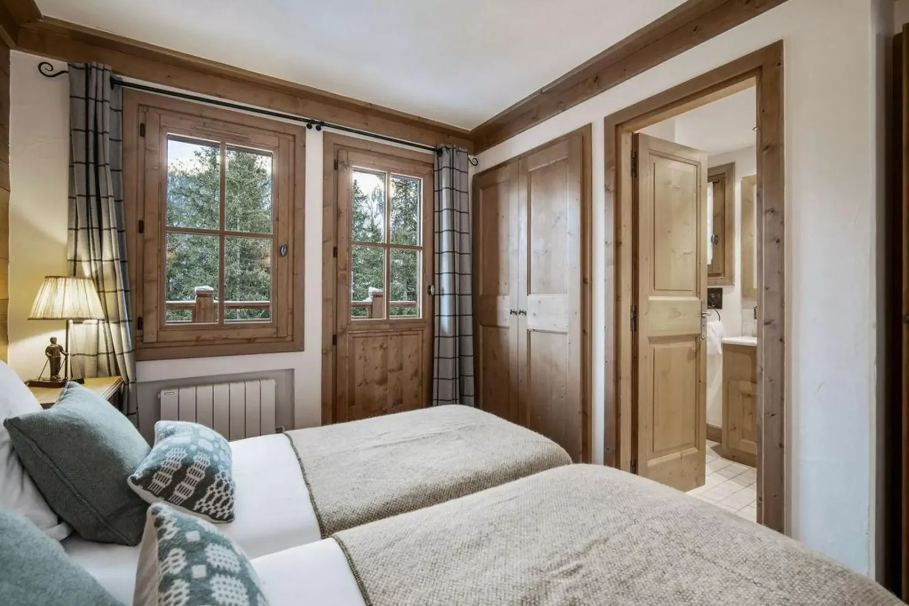 A bedroom with two beds beside wood-framed windows and an open doorway.