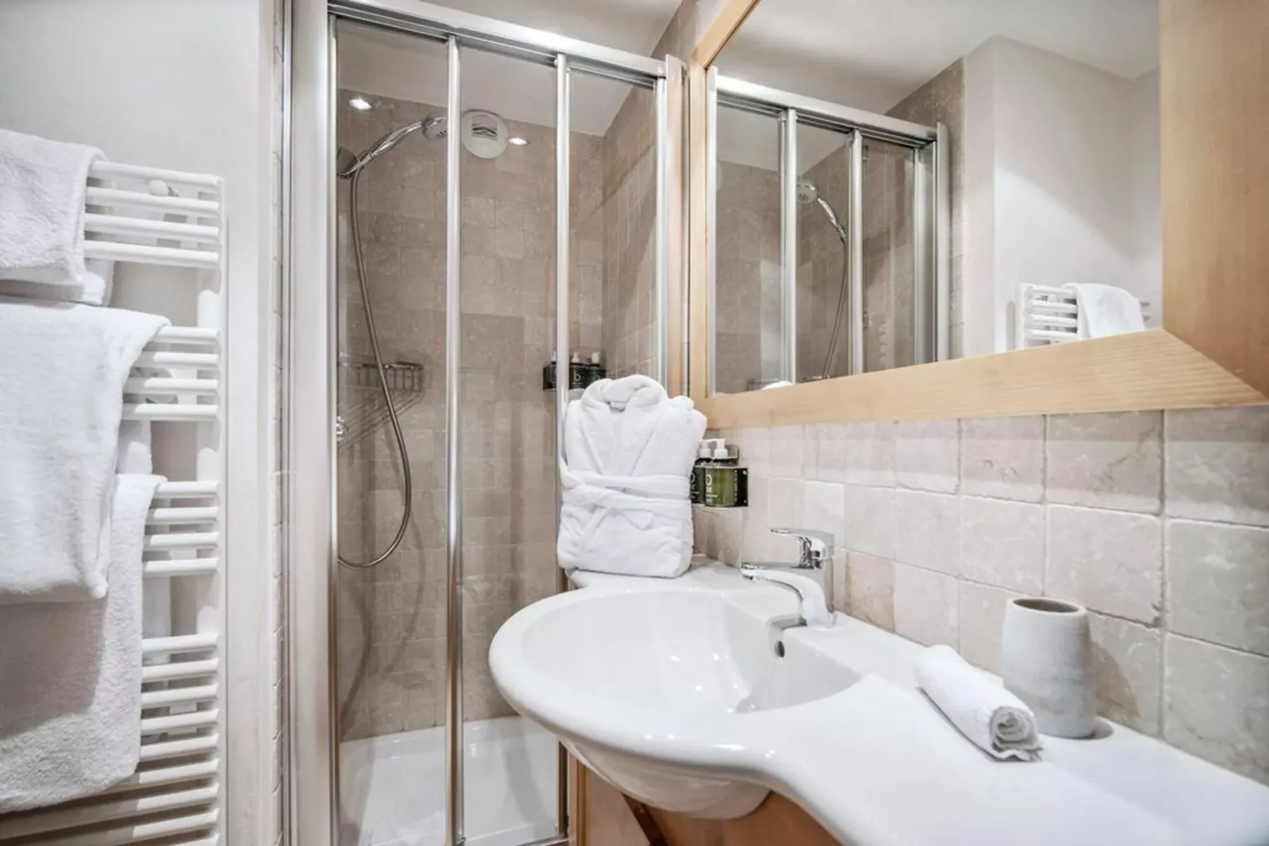 A tiled bathroom with a glass shower, sink, and towel warmer.