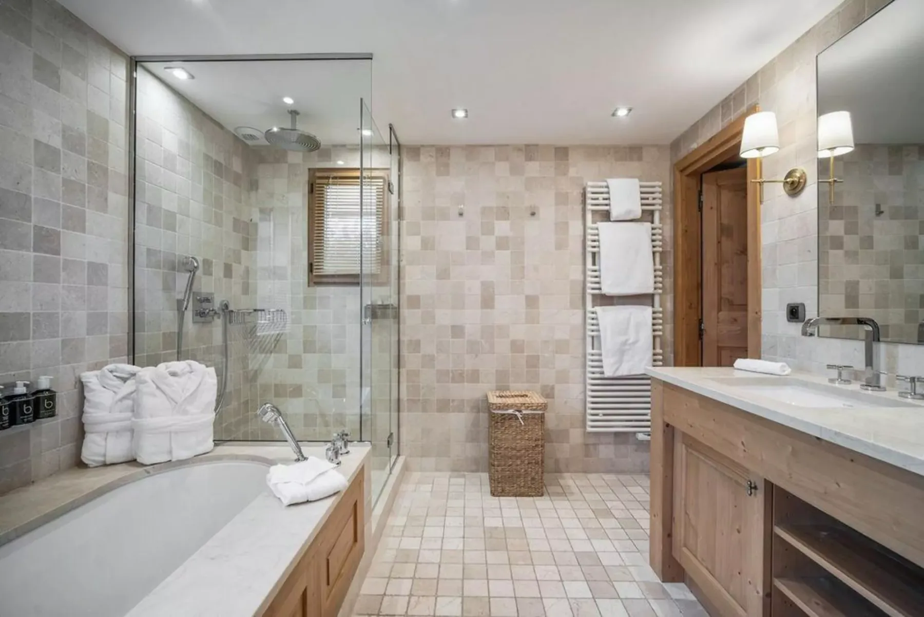 A spacious tiled bathroom with a bathtub, glass shower, and wooden vanity.