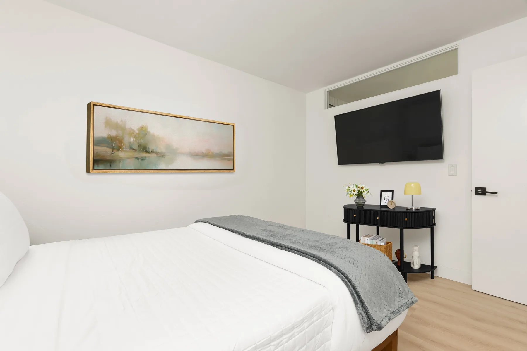 Un dormitorio con una cama bien tendida y un televisor montado en la pared.
