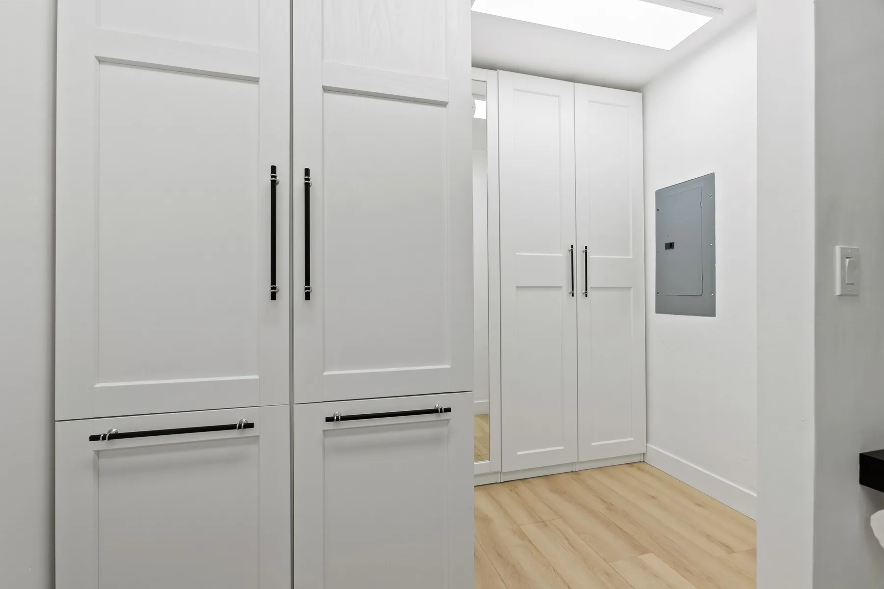 Un pasillo interior luminoso con armarios empotrados blancos y suelo de madera clara.