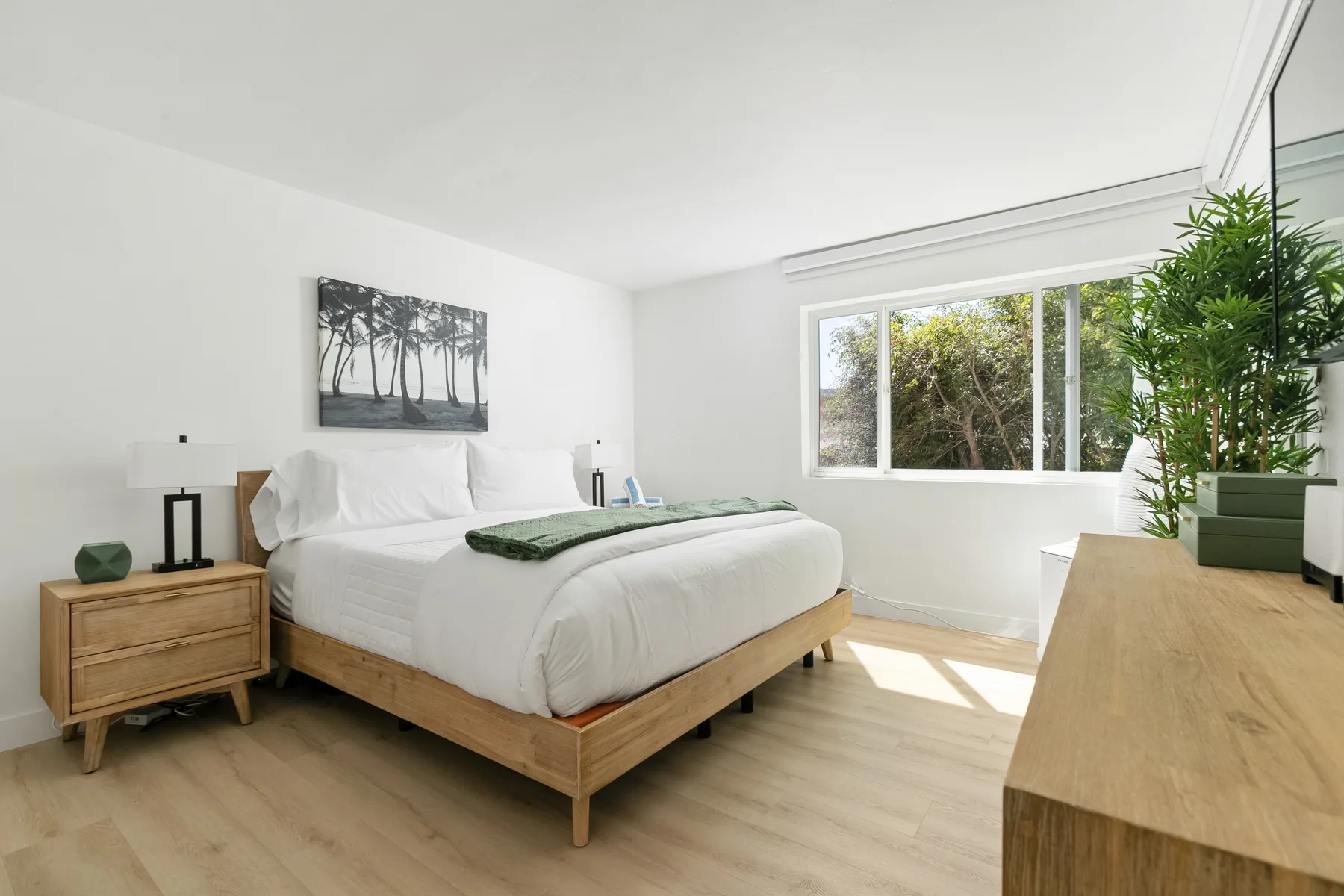 Un dormitorio luminoso con una cama, una mesita de madera y una ventana amplia.