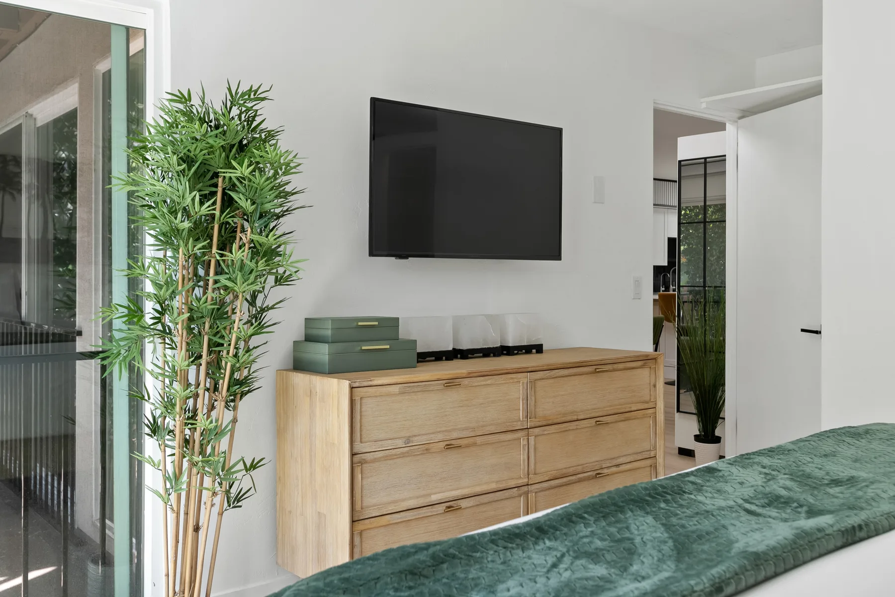 Un dormitorio con una cómoda de madera, un televisor montado en la pared y una colcha verde.