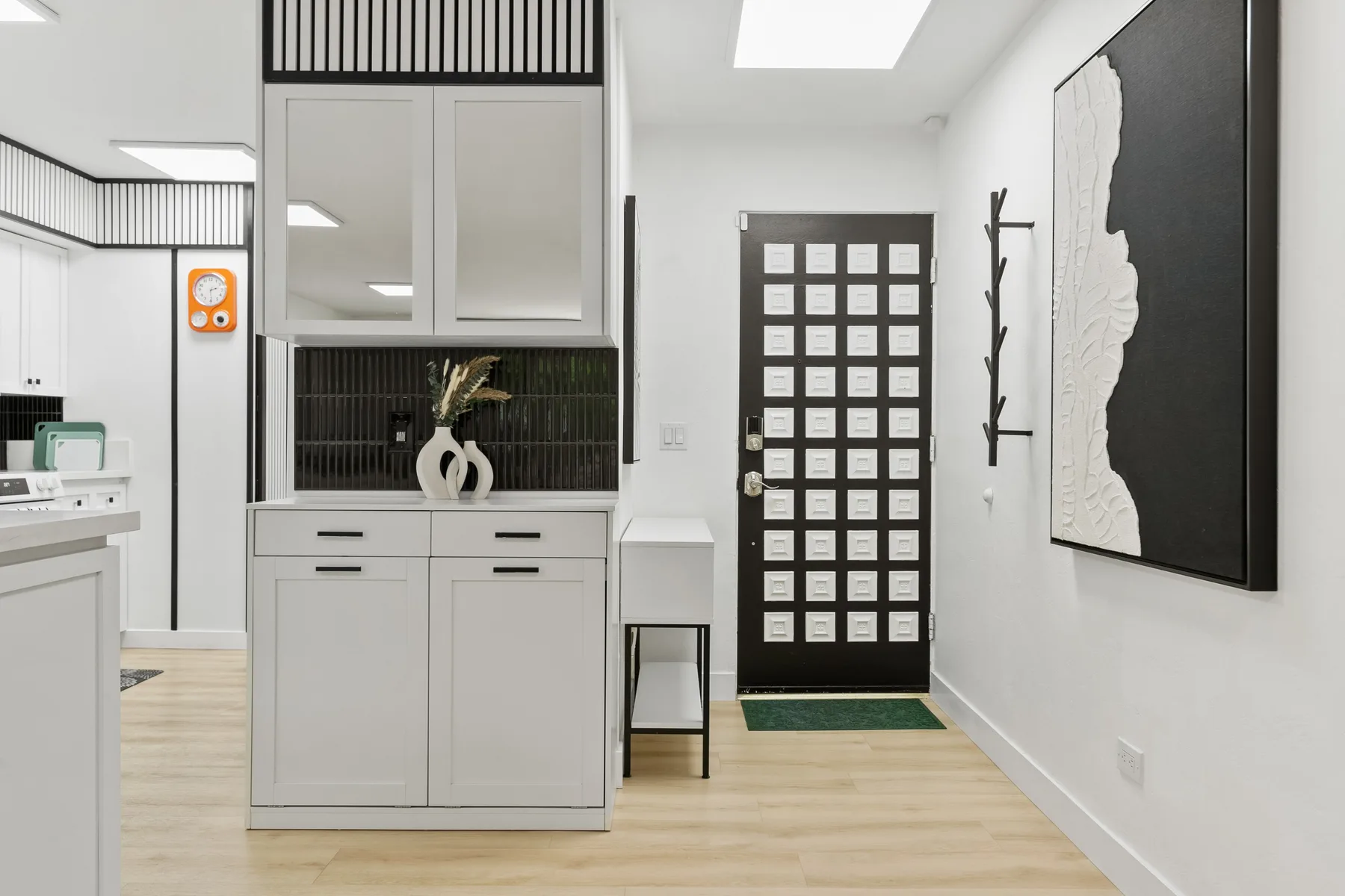 Un pasillo interior luminoso con una puerta de cuadrícula negra y suelo de madera clara.