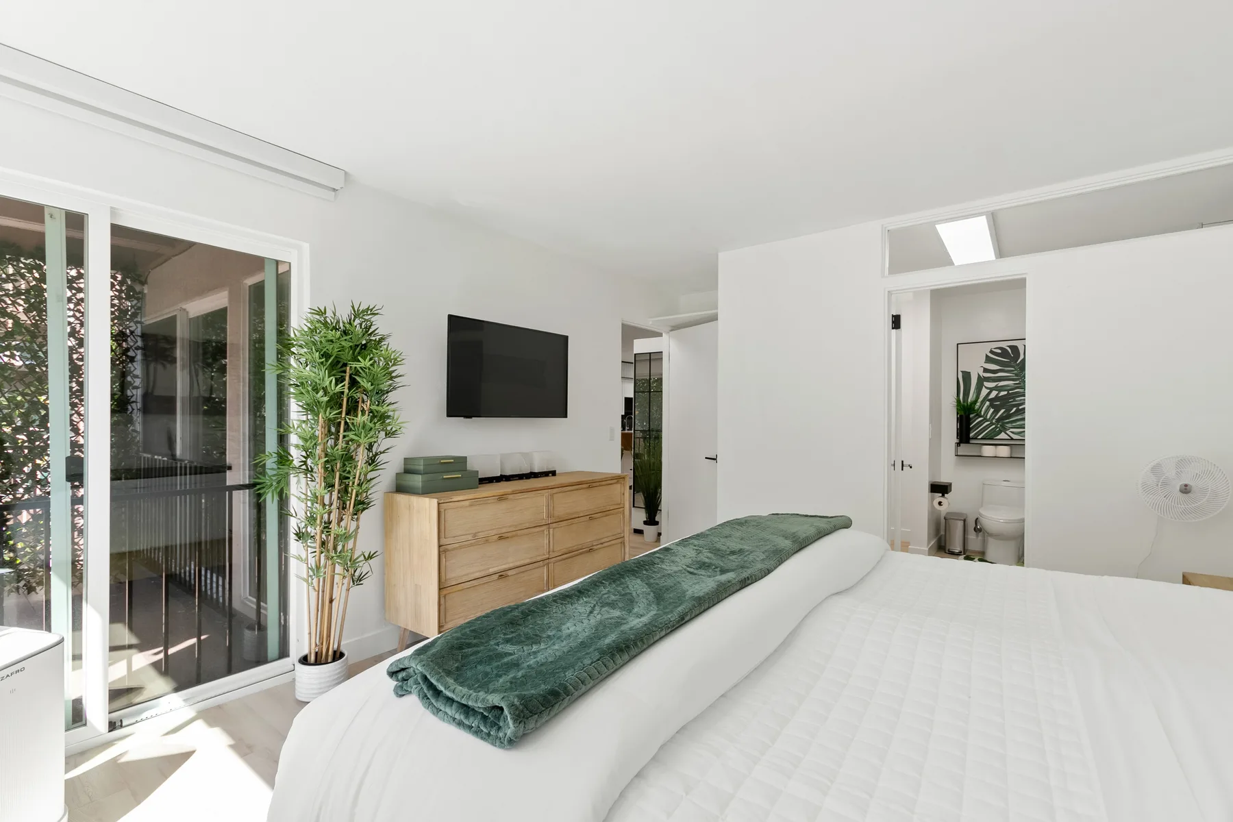 Un dormitorio luminoso con una cama, una cómoda y puertas corredizas de vidrio.