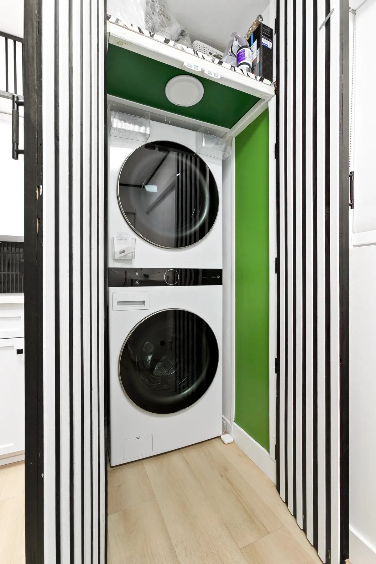 Un rincón de lavandería con lavadora y secadora apiladas junto a una pared verde.