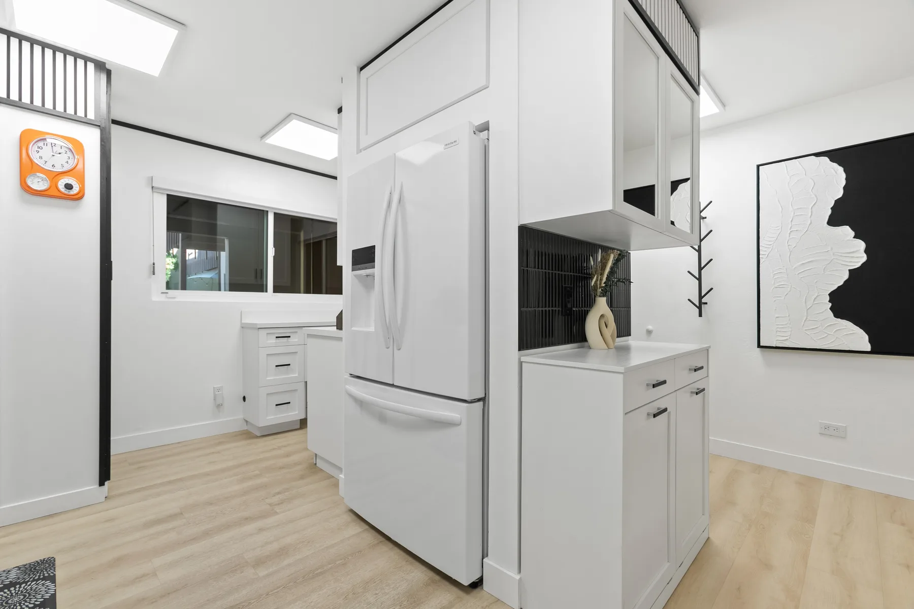 Una cocina luminosa con gabinetes blancos, un refrigerador y piso de madera clara.