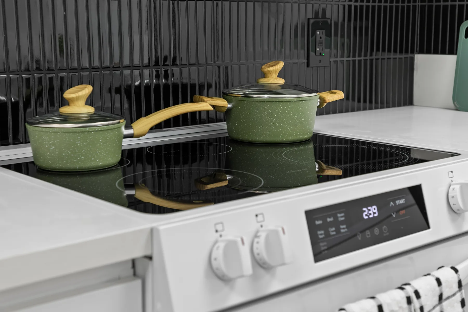 Una cocina con dos ollas verdes está junto a un salpicadero de azulejos oscuros.