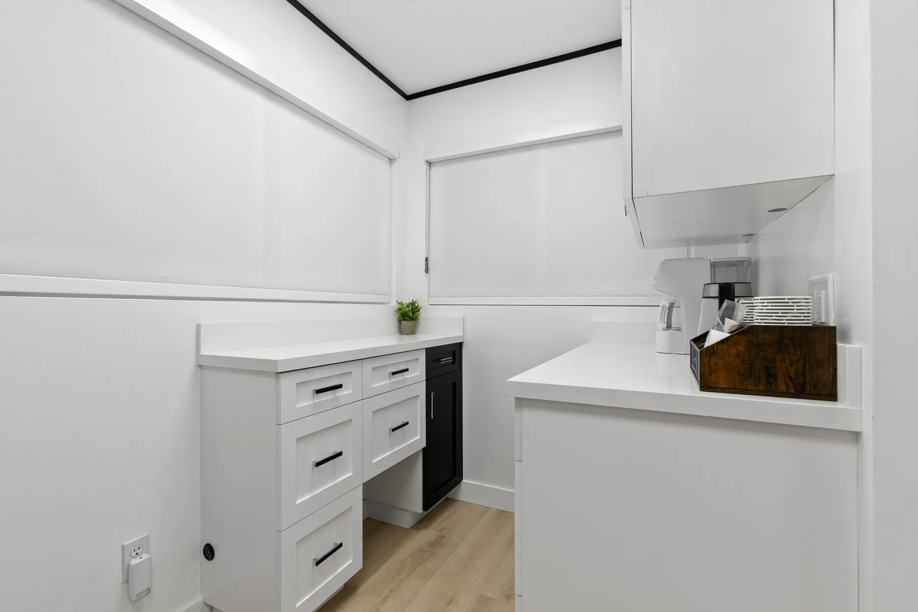 Una cocina luminosa con gabinetes blancos, encimeras y piso de madera clara.