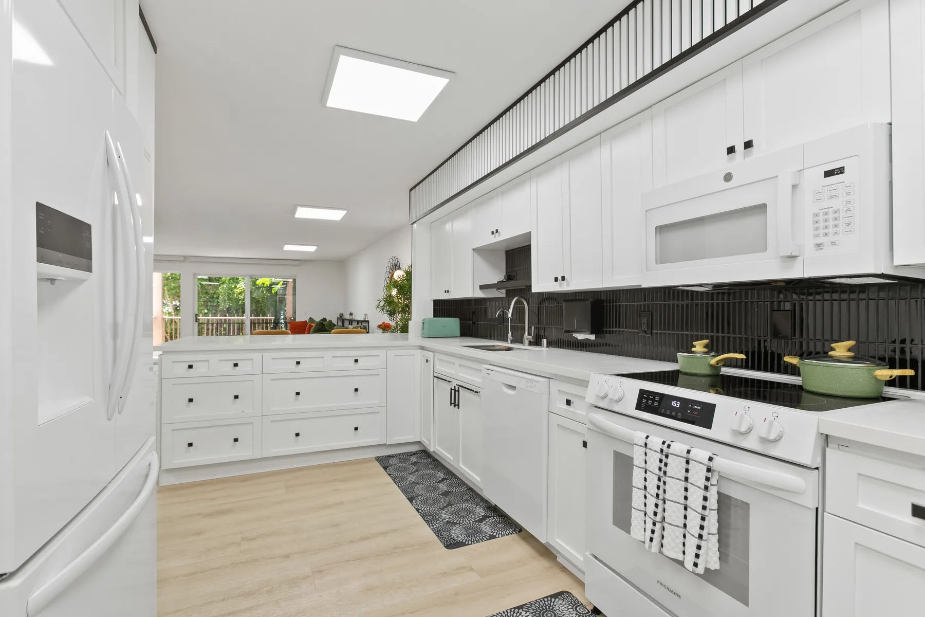 Una cocina blanca y luminosa con una encimera larga y electrodomésticos.