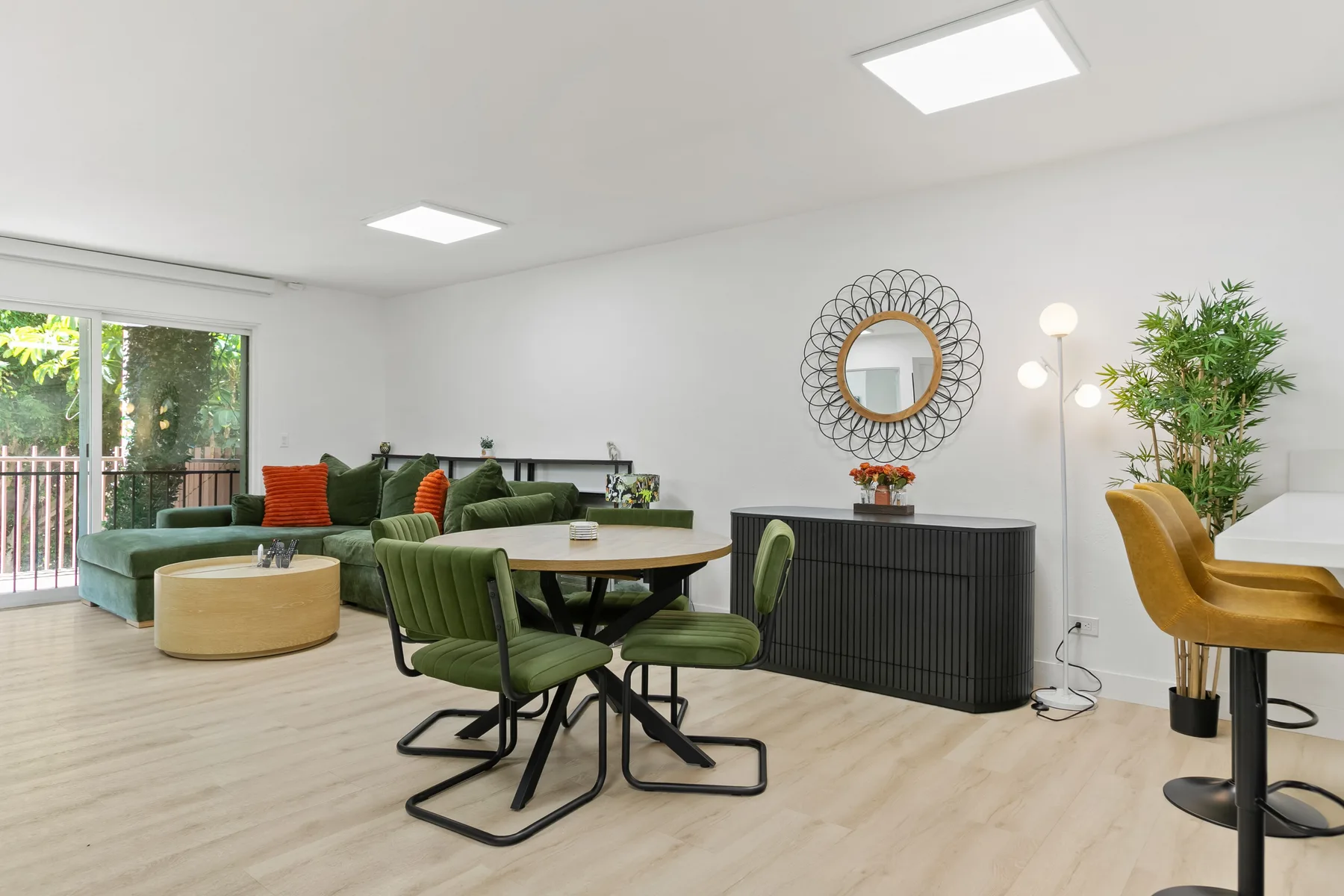 Una luminosa zona de comedor y estar con asientos verdes y una mesa redonda.