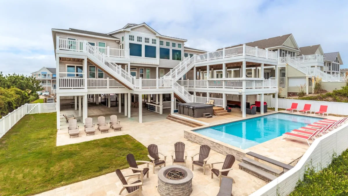 A large coastal-style house overlooks a swimming pool and outdoor seating area.