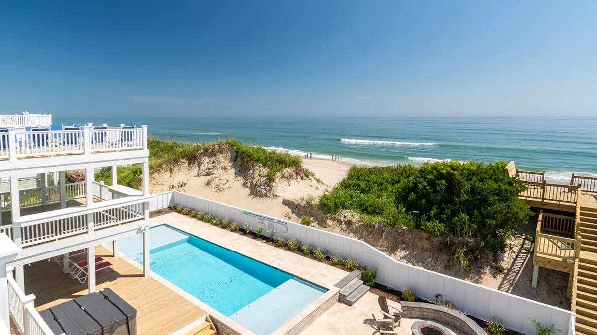 A coastal pool area overlooks sandy dunes and the ocean.