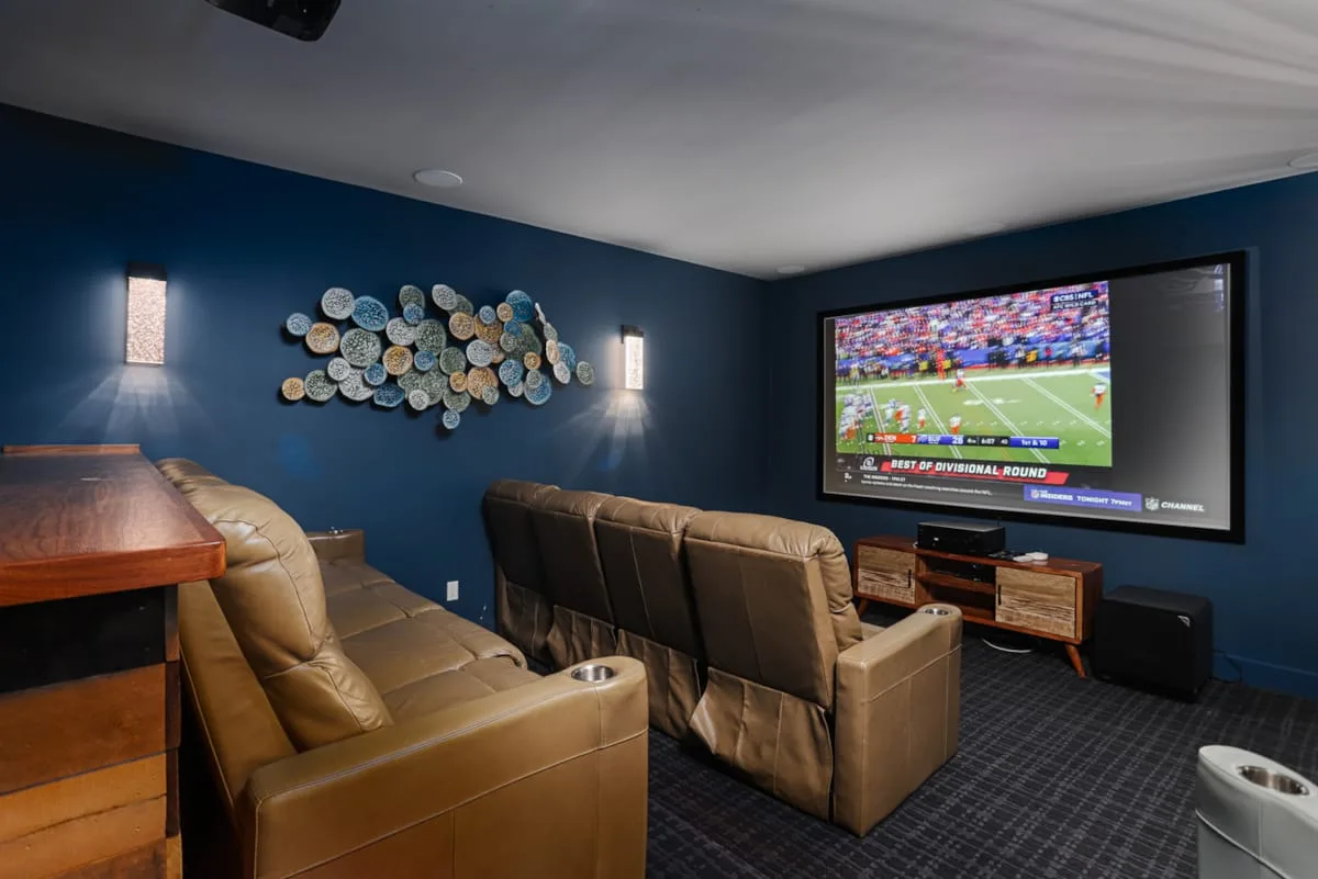 A home theater with rows of seating facing a large screen showing a football game.
