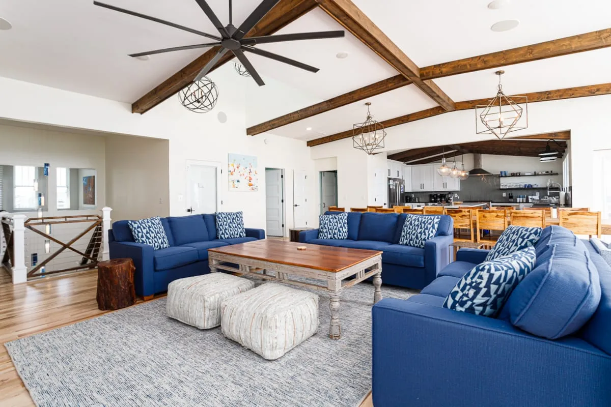 A living room with blue seating, a large coffee table, and exposed ceiling beams.
