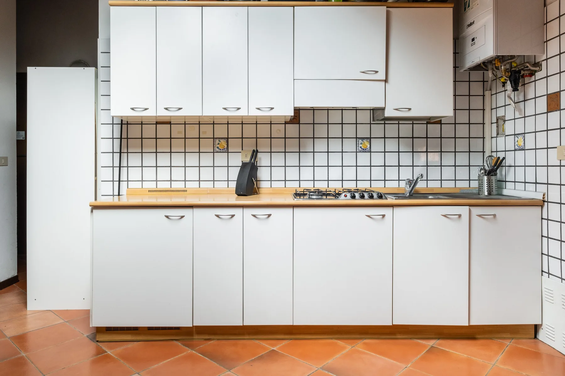 Una cocina luminosa con gabinetes blancos, paredes de azulejos y una placa de cocina.