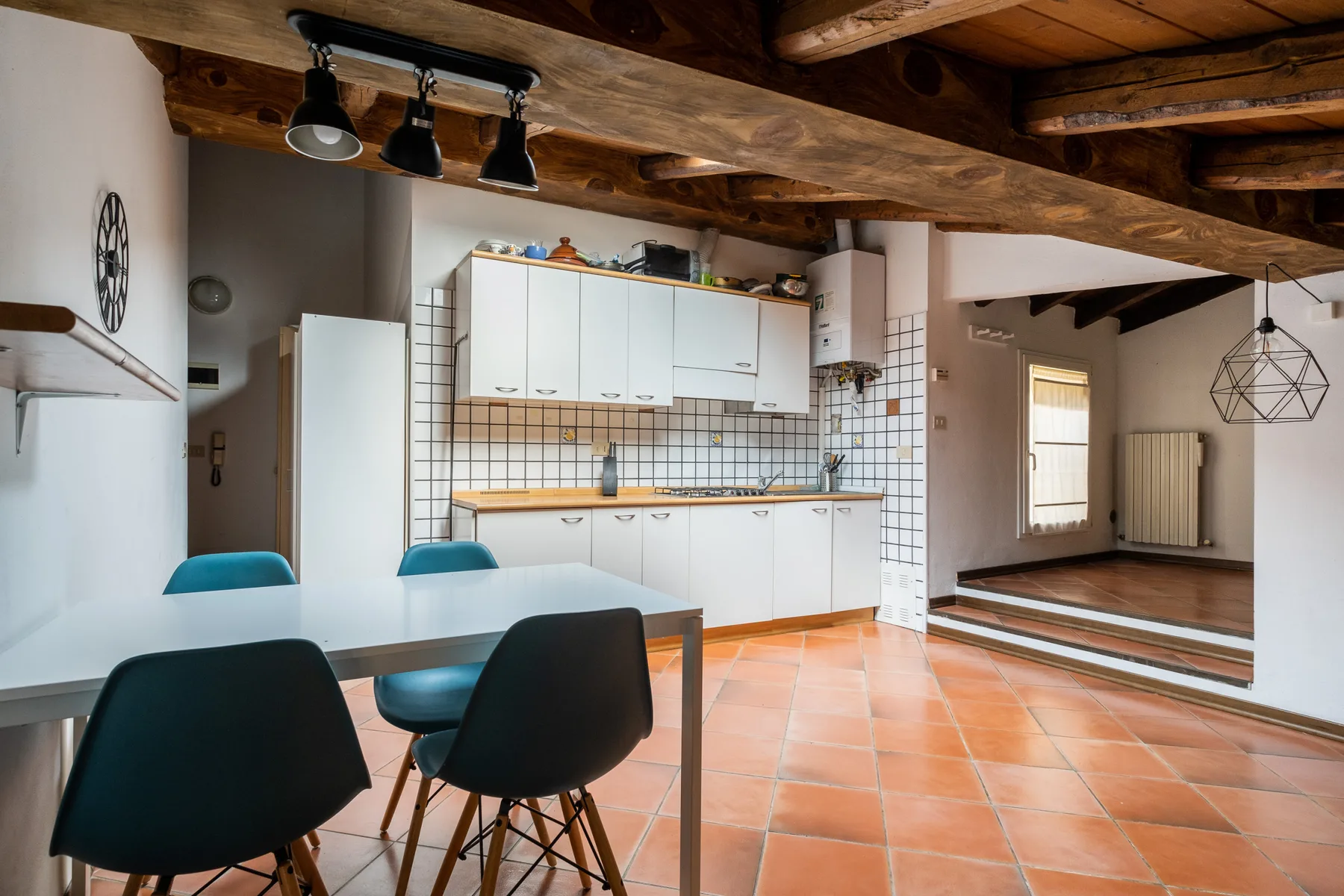 Una cocina y comedor con armarios blancos, una mesa y vigas de madera a la vista.