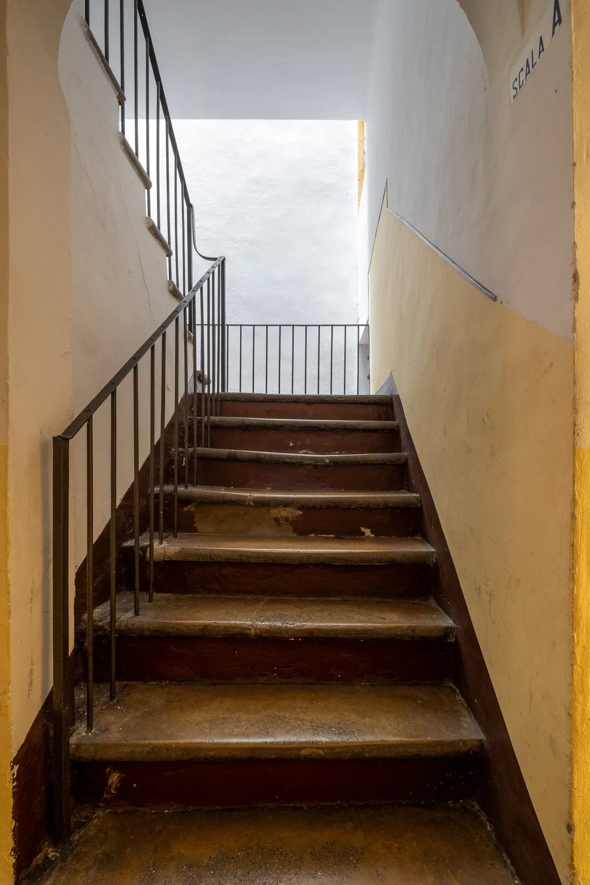 Una estrecha escalera interior con barandillas oscuras conduce a un rellano luminoso.