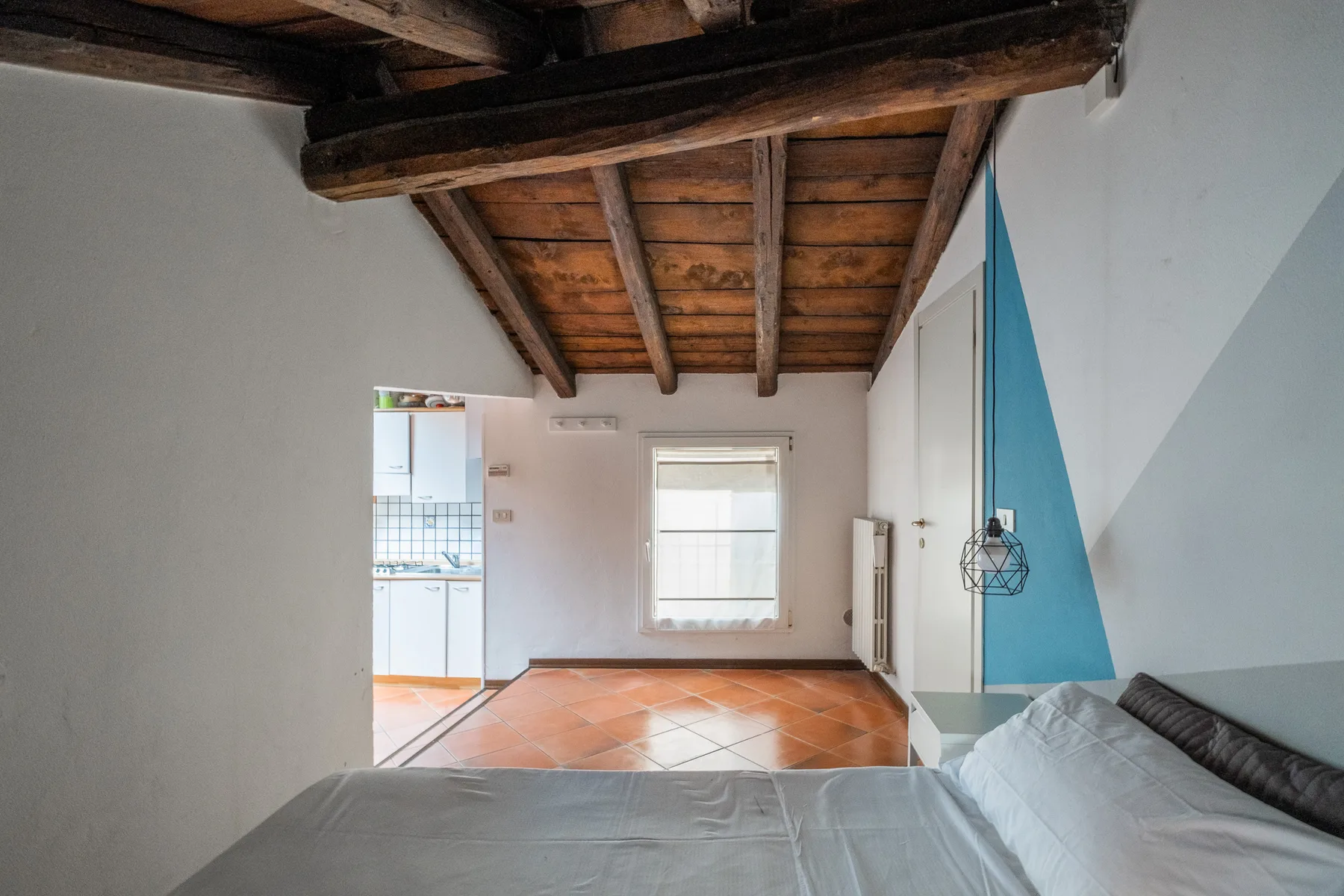 Un dormitorio con una cama bajo un techo de madera expuesta y una ventana.