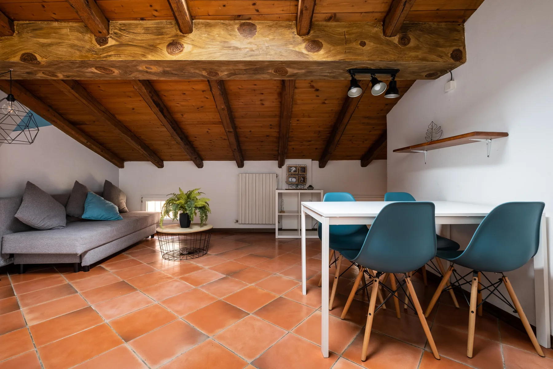 Zona de comedor y estar con una mesa blanca, asientos azul verdosos y un sofá gris.