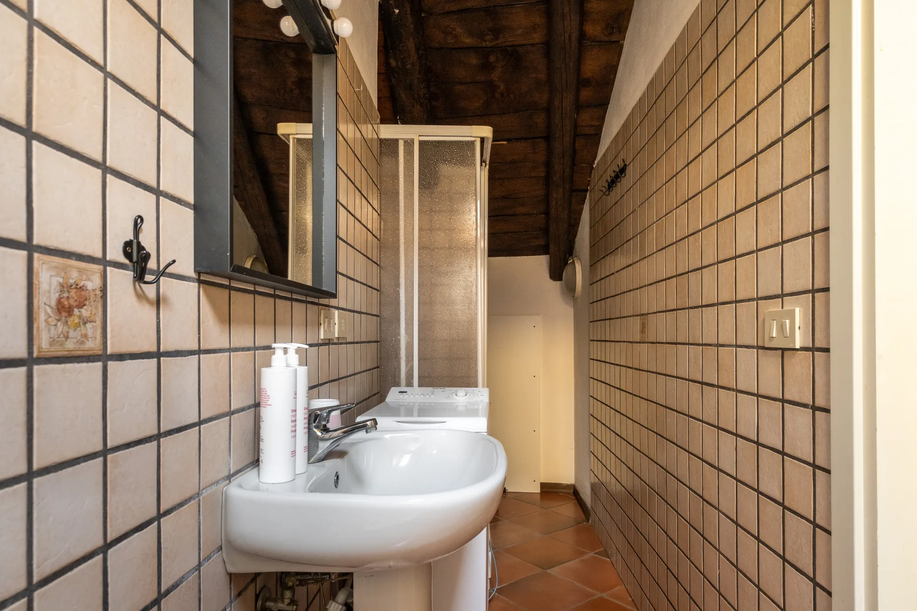Un baño estrecho con un lavabo de pared y una ducha al fondo.