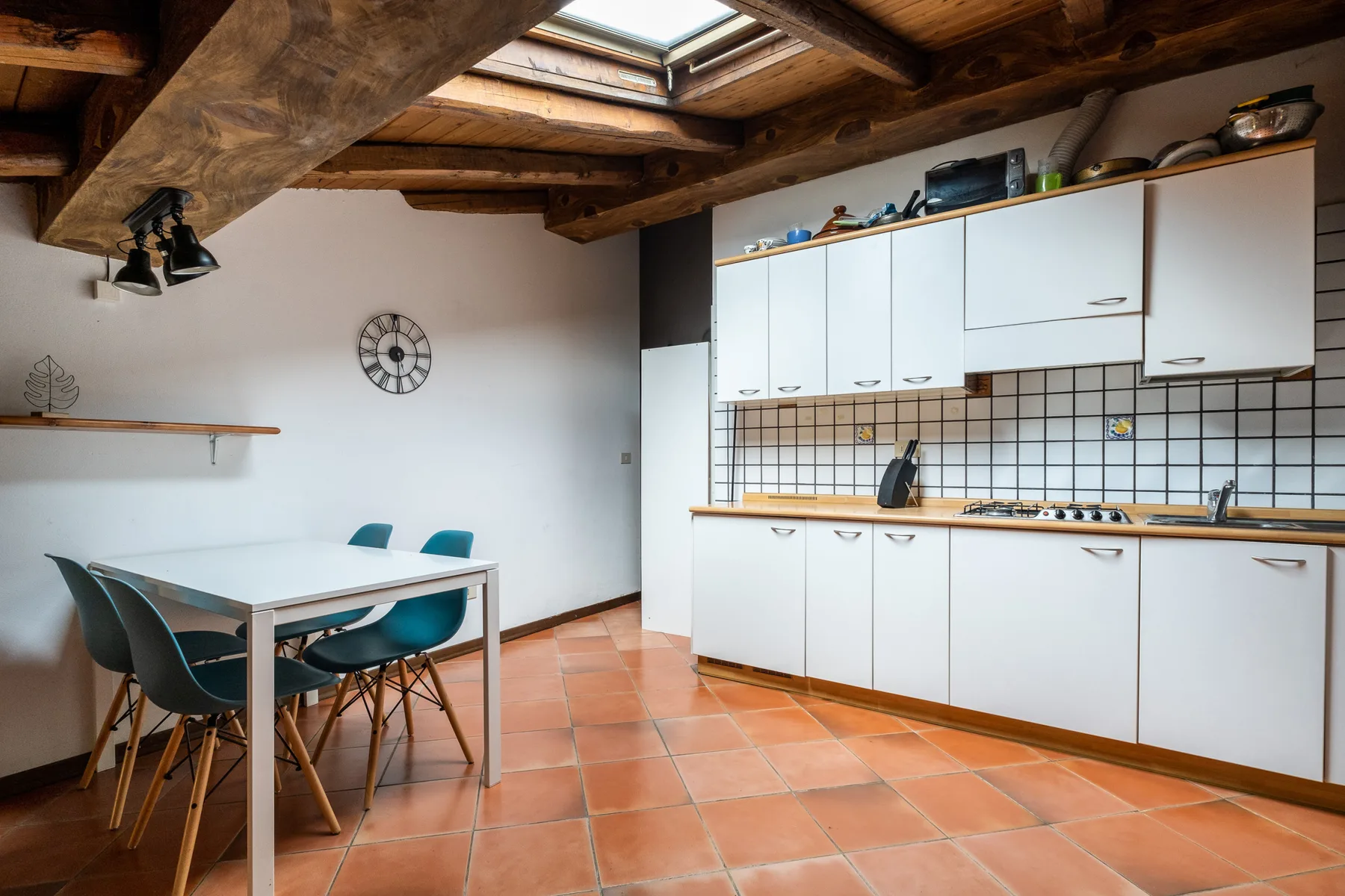 Una cocina y comedor con armarios blancos, una mesa y vigas de madera expuestas.