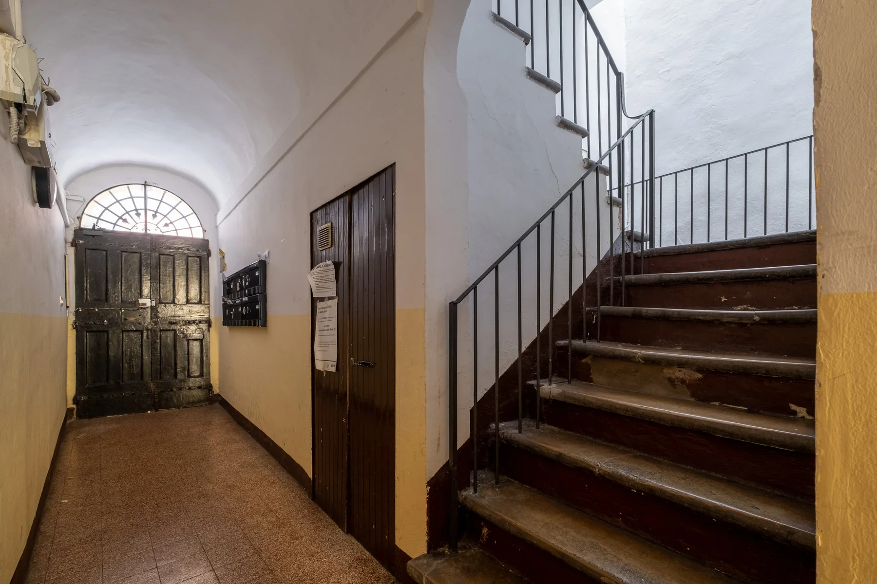 Un pasillo interior con una puerta de entrada de madera oscura y una escalera.