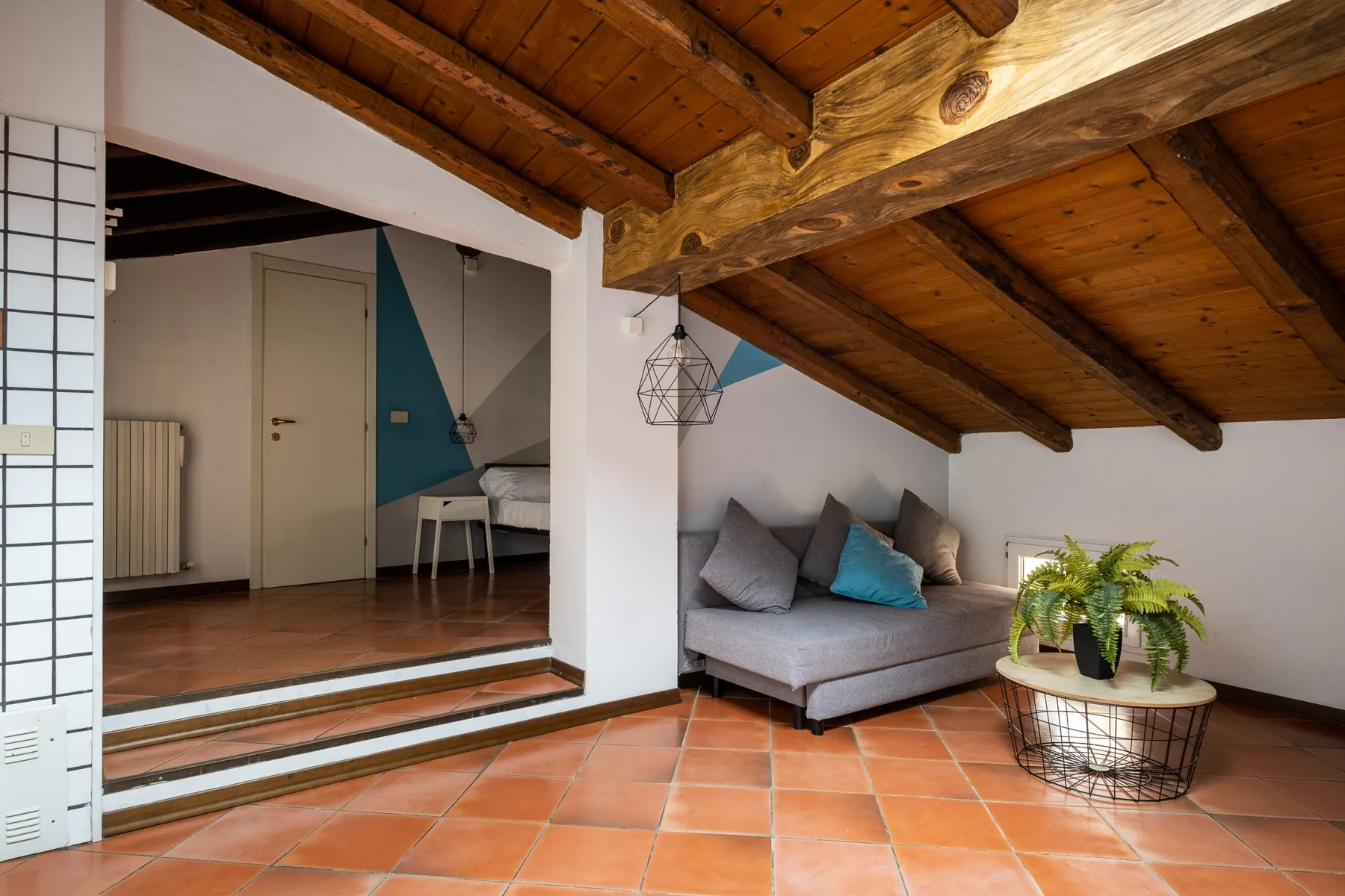 Una sala tipo loft con un sofá seccional gris y una planta bajo un techo inclinado de madera.