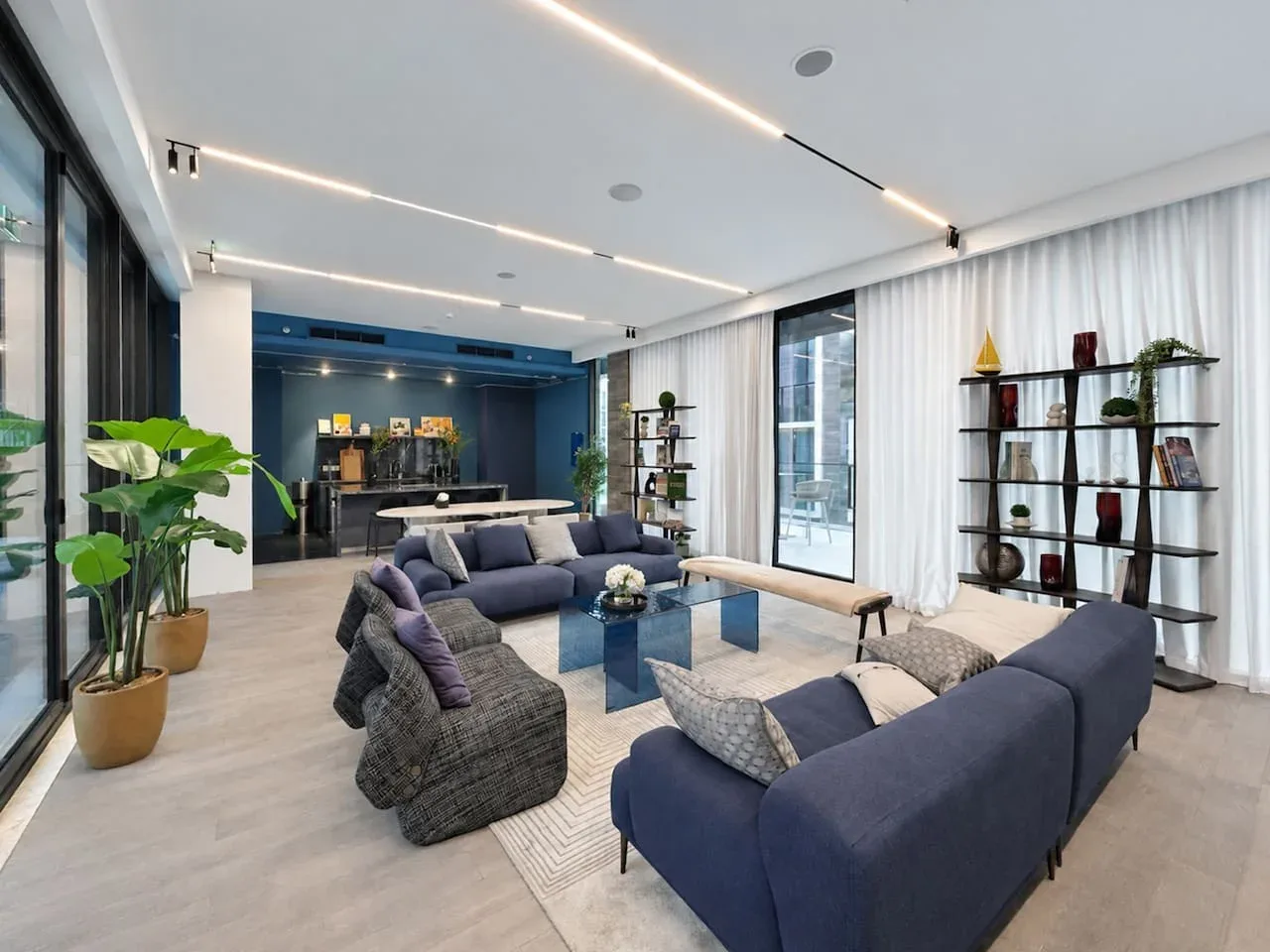 A modern living room with blue seating, a glass coffee table, and large windows.