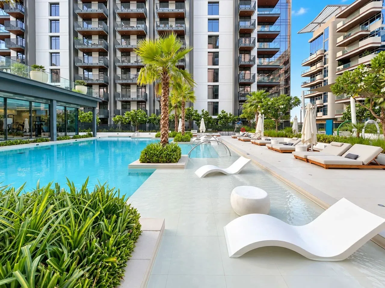An outdoor swimming pool with lounge seating and modern apartment buildings in the background.
