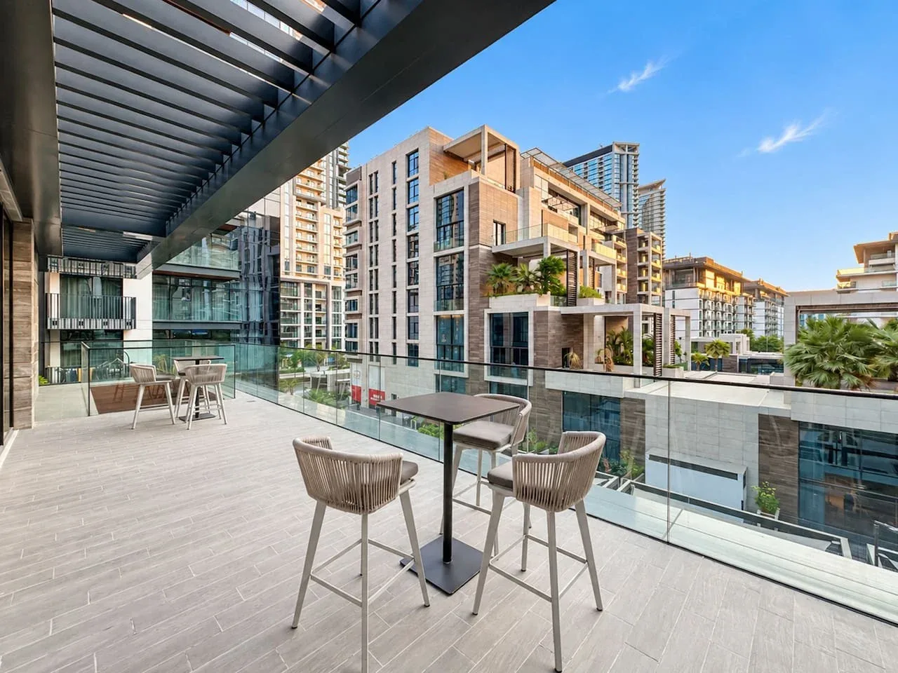 An outdoor terrace with seating and a glass railing overlooks nearby buildings.