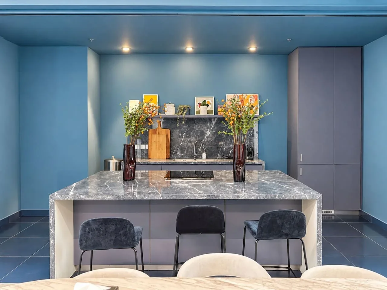A blue-toned kitchen with a large island, dark countertops, and seating.